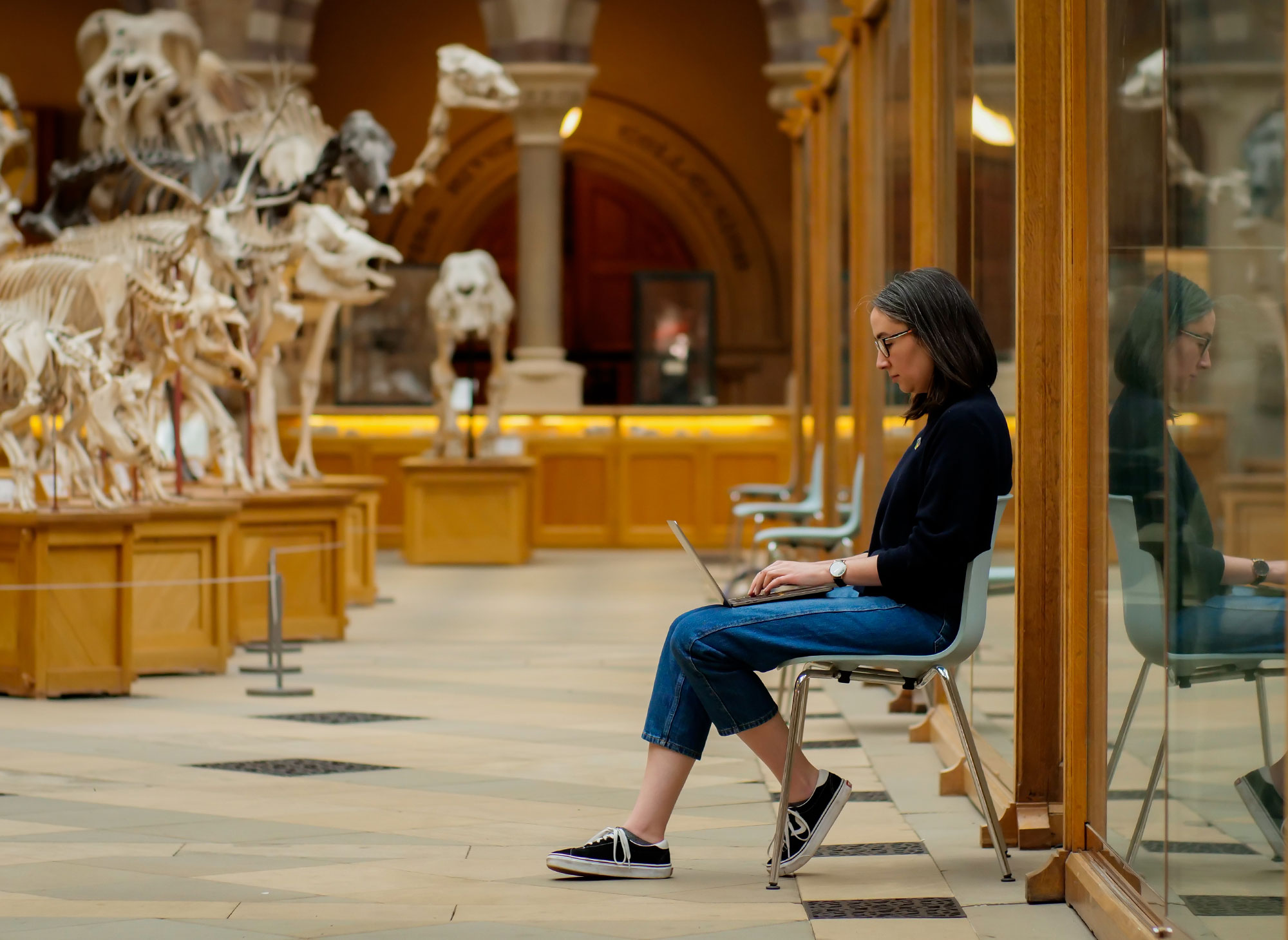 A woman working on a laptop at a natural history museum with animal skeletons in the background.