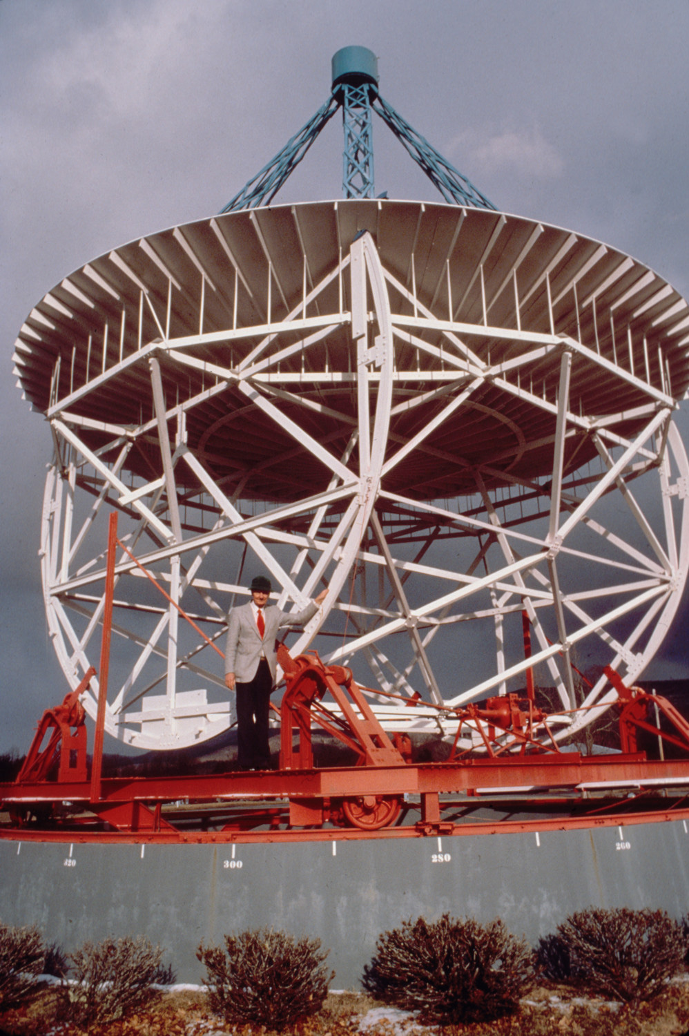 Photo of a large white and orange radio antenna with a Grote Reber standing in front of it