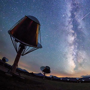 Photo of radio telescopes at the Allen Telescope Array with a starry sky featuring the Milky Way in the background.