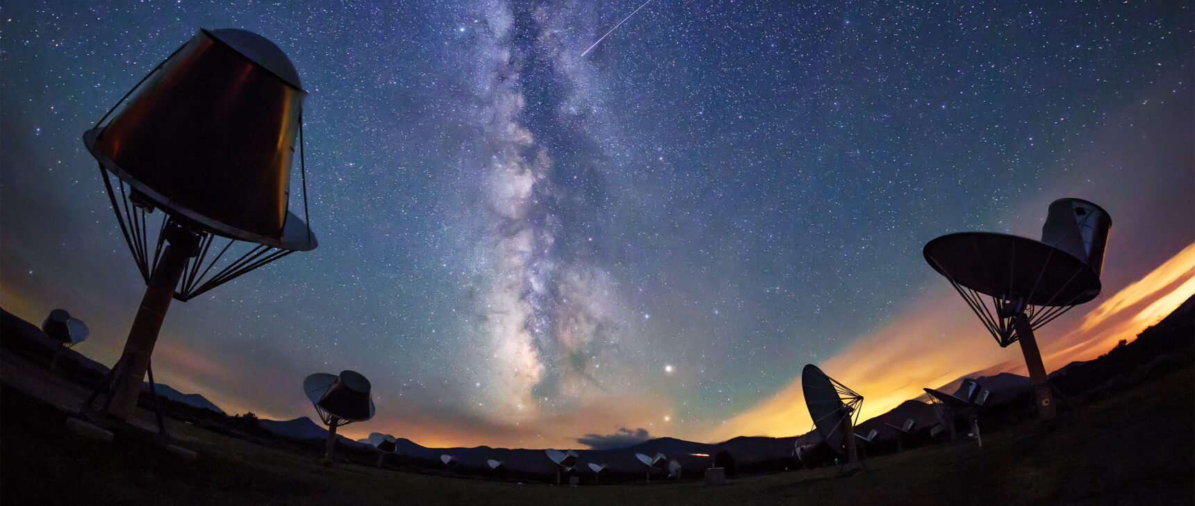 Photo of radio telescopes at the Allen Telescope Array with a starry sky featuring the Milky Way in the background.