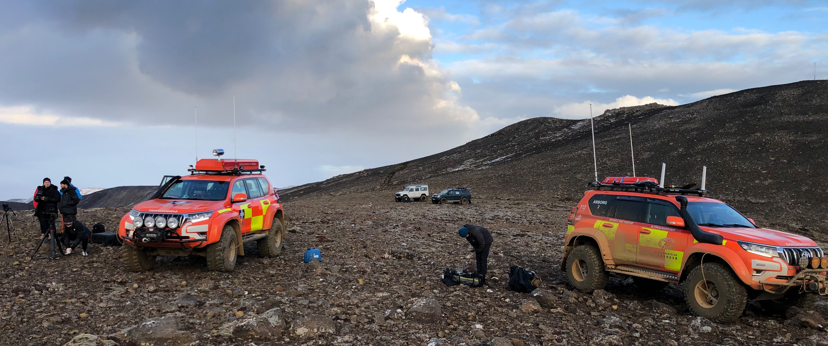 Two bright orange off-road vehicles on a lava field.