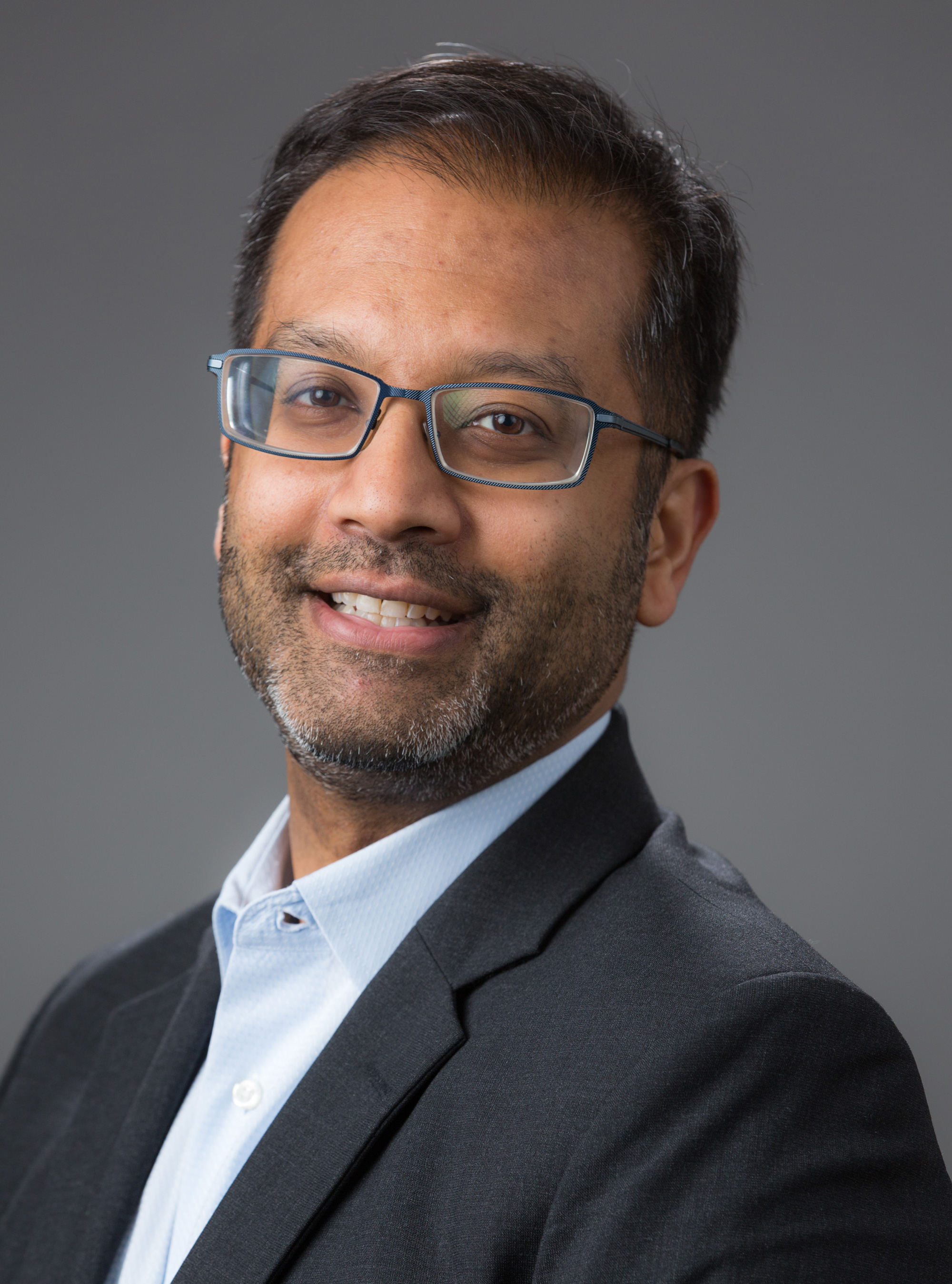 Samit Dasgupta in a suit jacket against a dark background