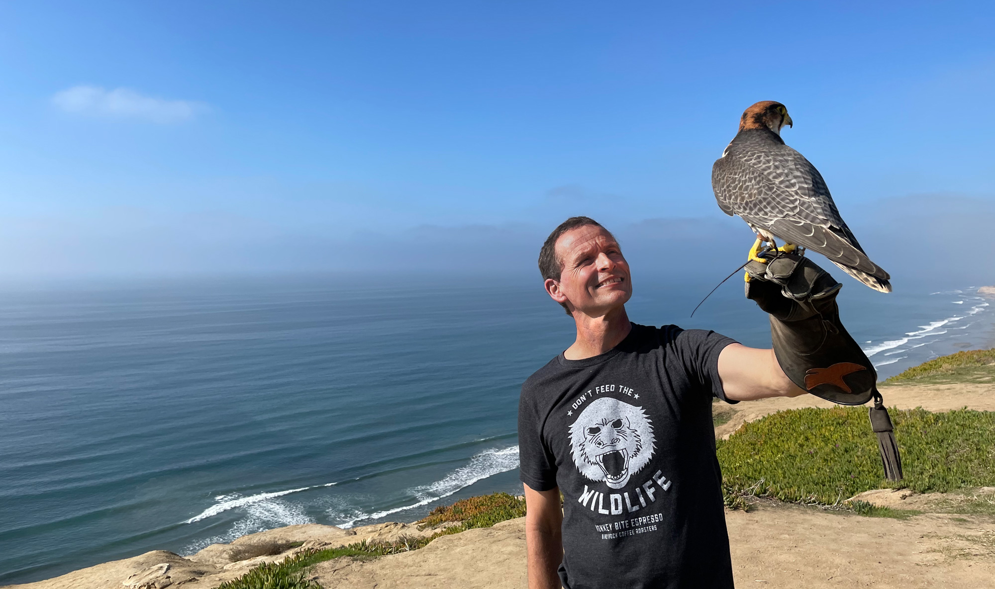 Photo of the evolutionary biologist Pierre Gagneux of the University of California, San Diego, posing near a beach while holding a falcon.