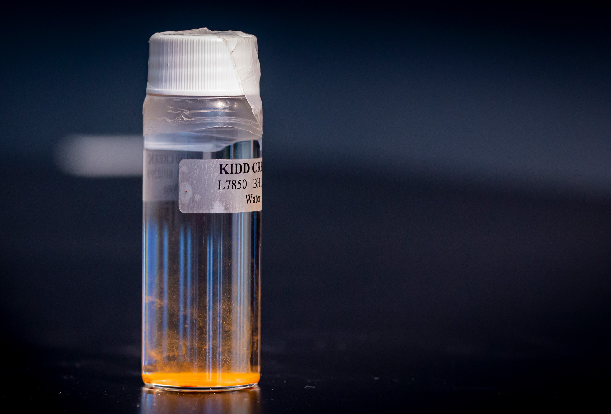 A labeled vial of water with some colored sediment near the bottom.