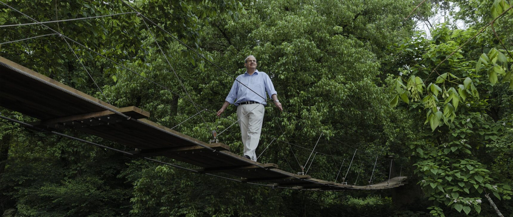 Color photo of Nathan Seiberg crossing a small wooden bridge in the woods.