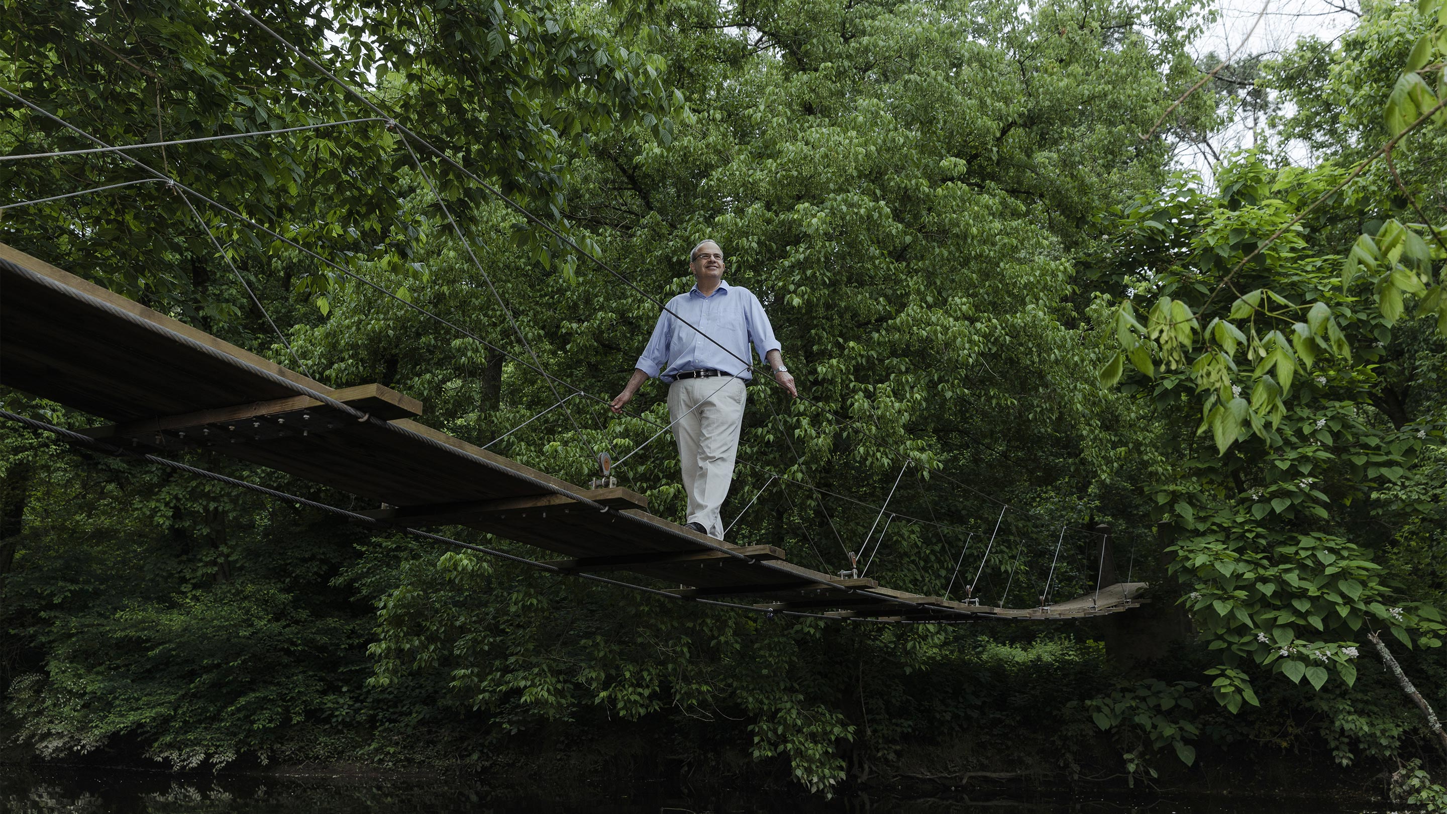 Color photo of Nathan Seiberg crossing a small wooden bridge in the woods.