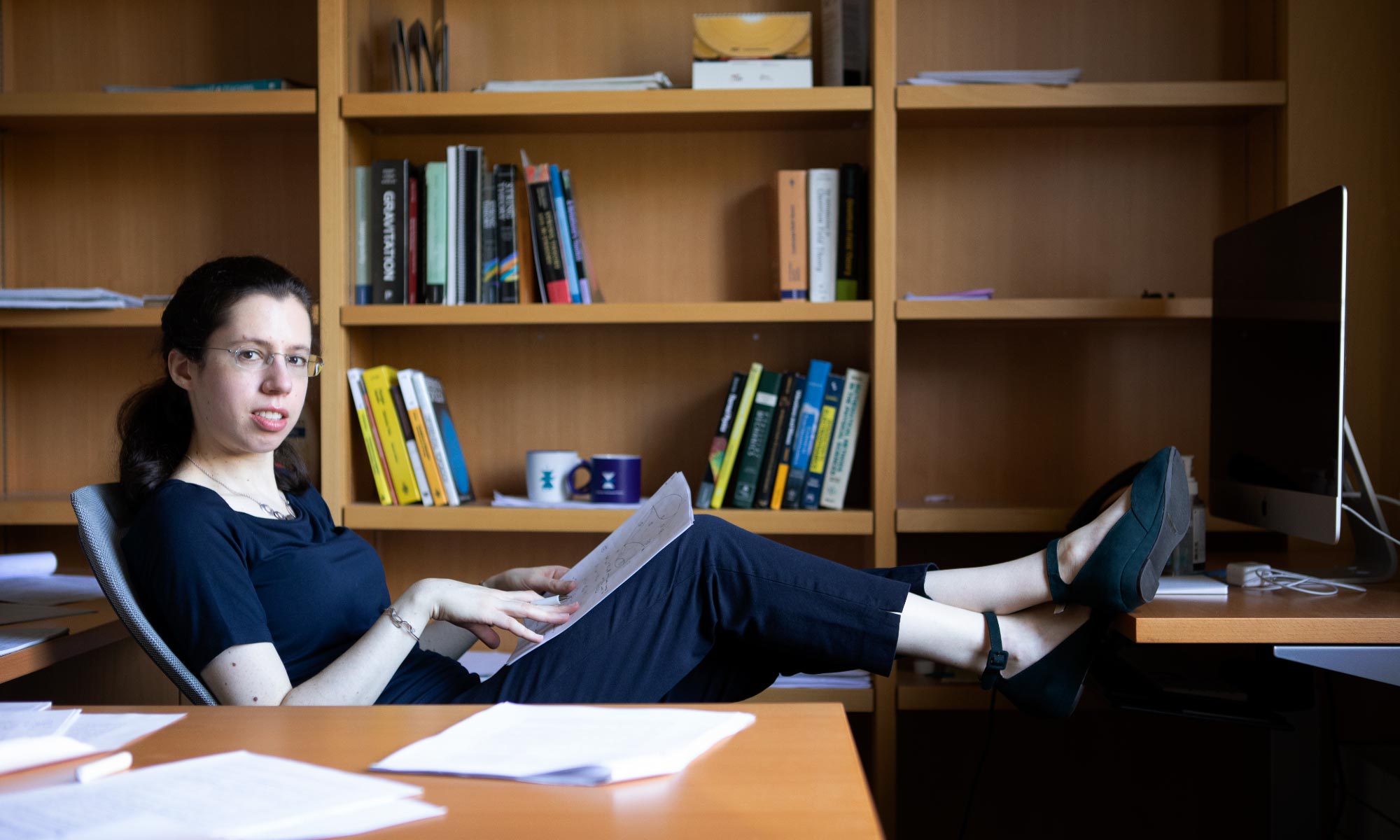 Photo of Engelhardt with her feet up on her desk glancing sideways at the camera with bookcases lining the wall behind.