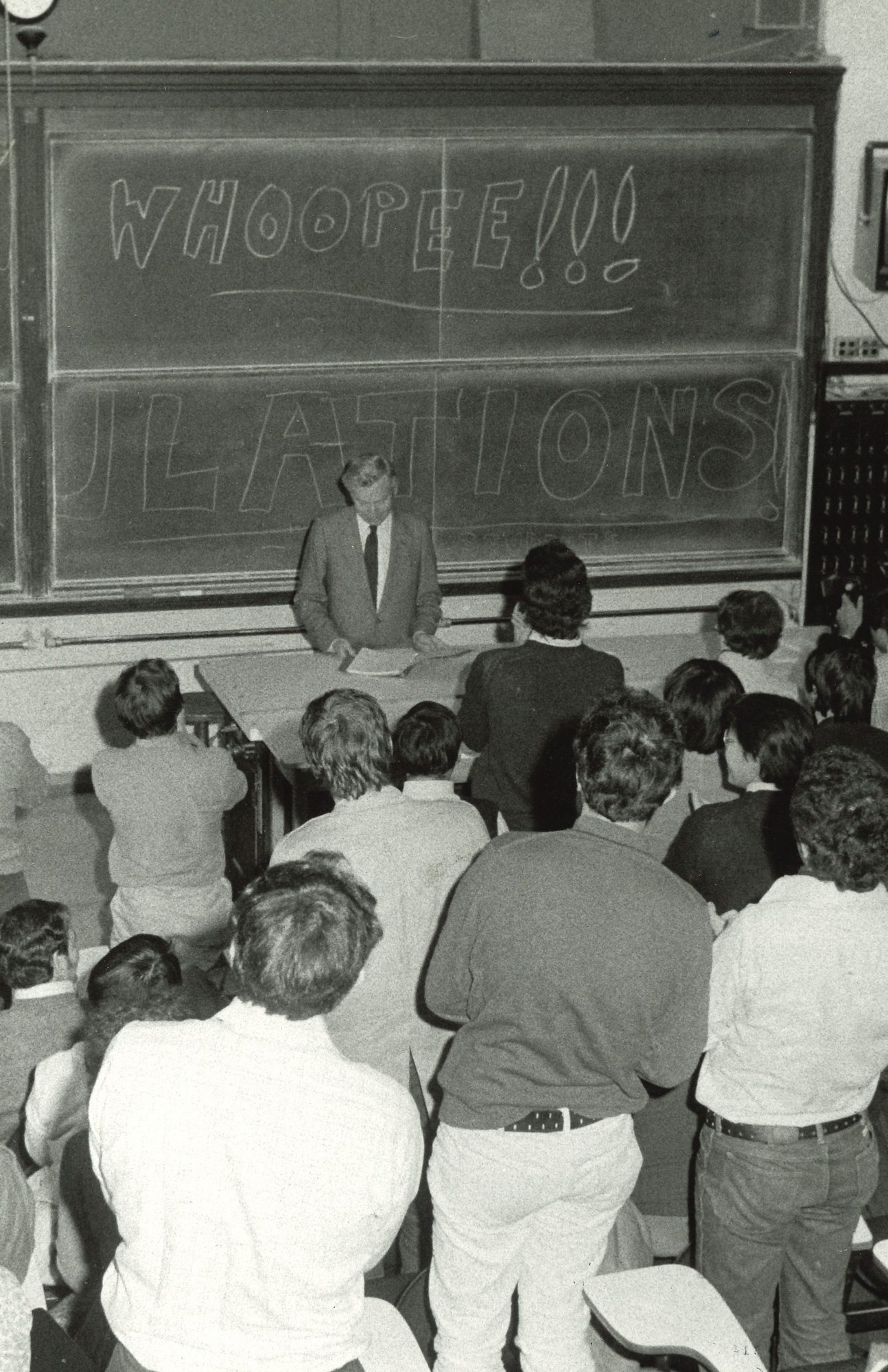 Black and white photo of Steven Weinberg in a classroom full of cheering, clapping college students