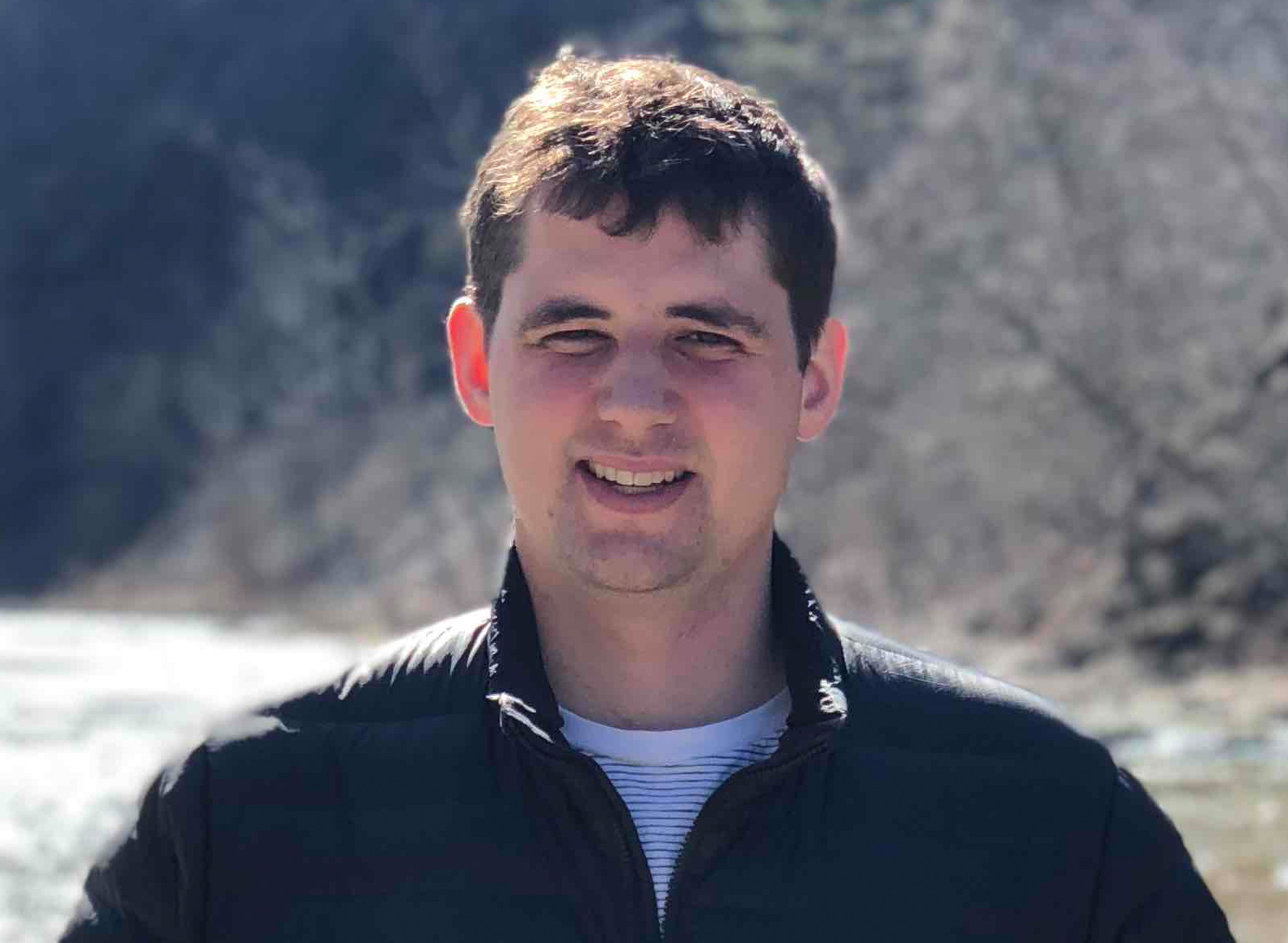 Photo of Austin Benson in a black coat in front of a river