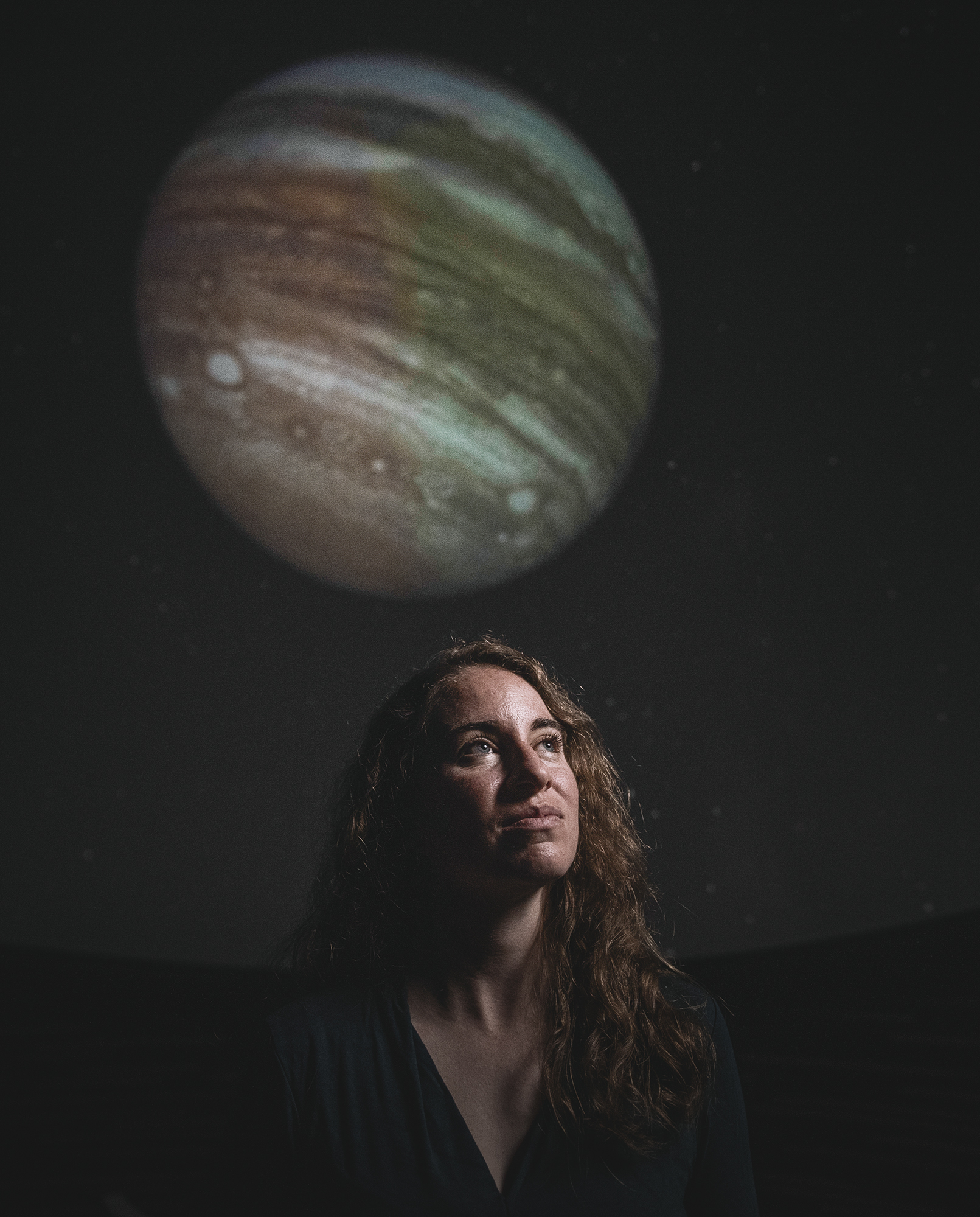 Kreidberg stands below a photograph of Jupiter.