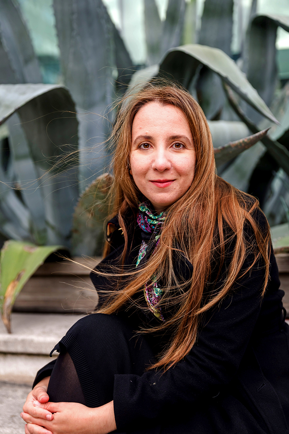 Outdoor photo of Ana Caraiani sitting in front of a big plant