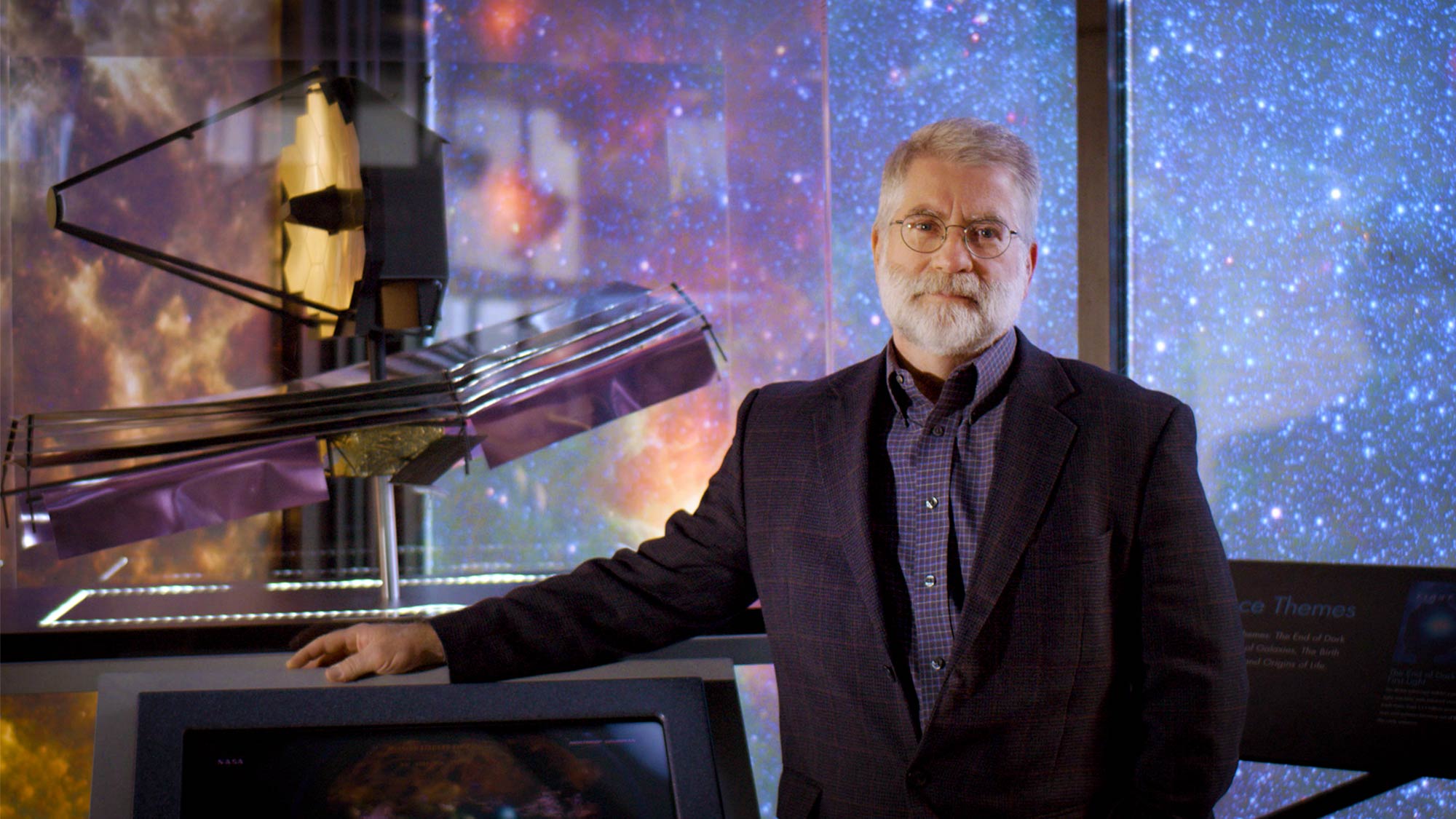 A man with a beard next to a model of a space telescope.