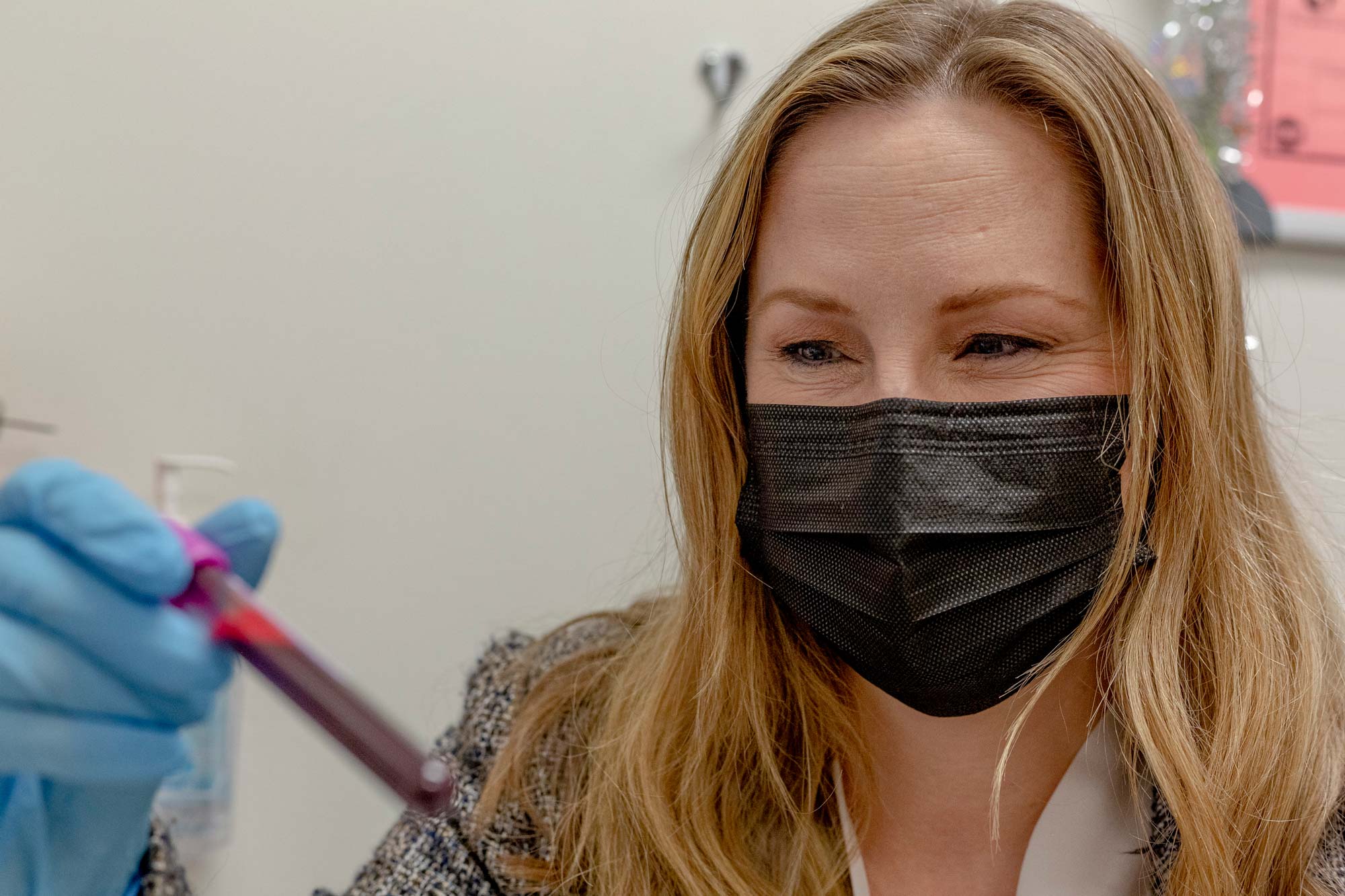 Cristen Willer of the University of Michigan, masked, holds a test tube full of blood.