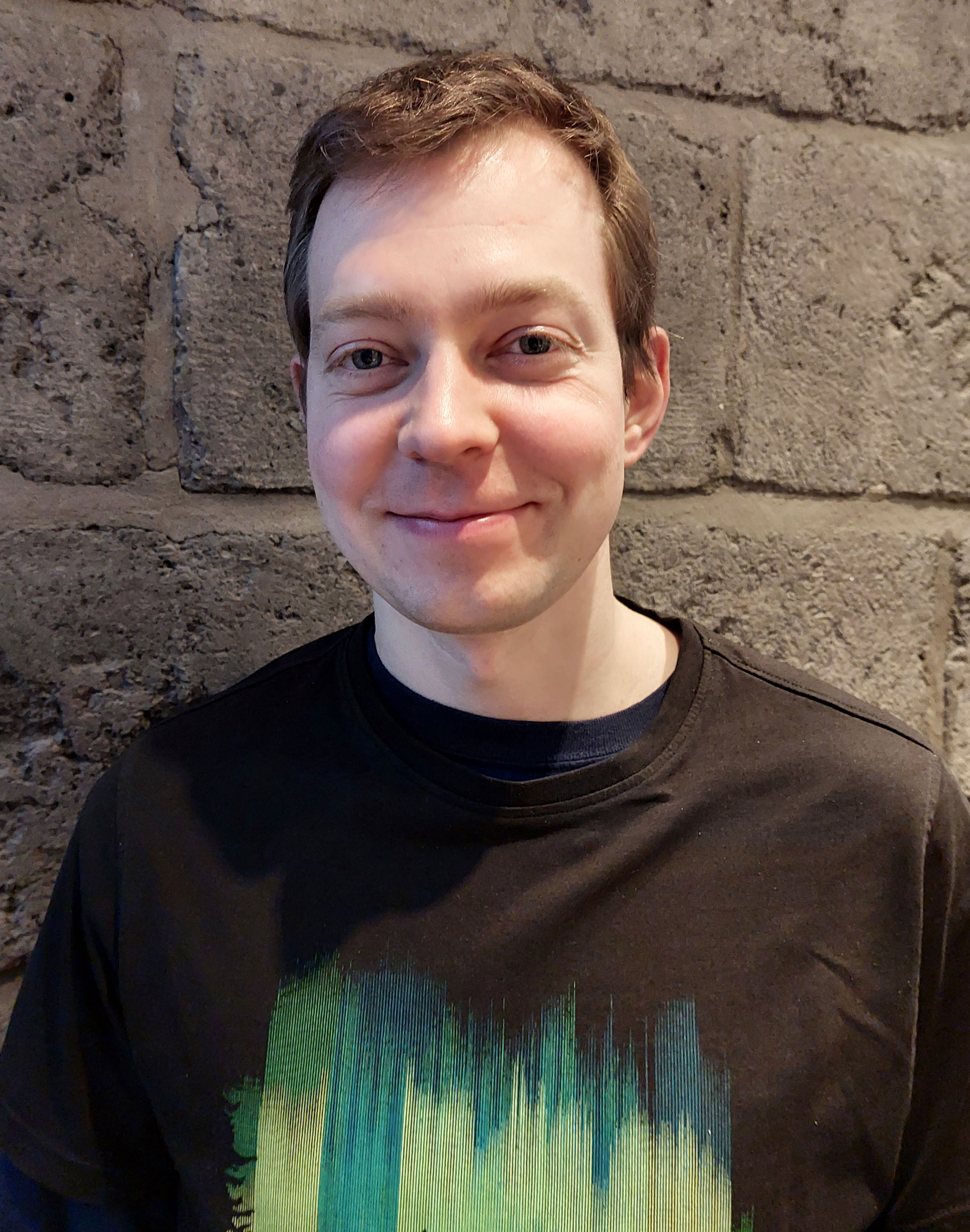 Color photo of Boris Knyazev in a black and green shirt in front of a stone wall