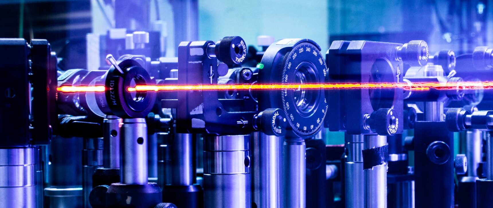 Photo of an array of metal tubes and glass pieces, with an orange laser cutting horizontally across