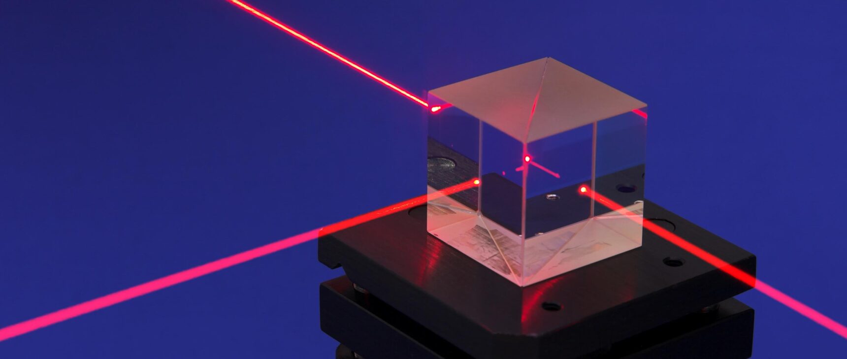 A red laser beam enters a glass cube and splits in two; half of the beam continues straight ahead and the other half shoots out of the glass cube at a right angle.