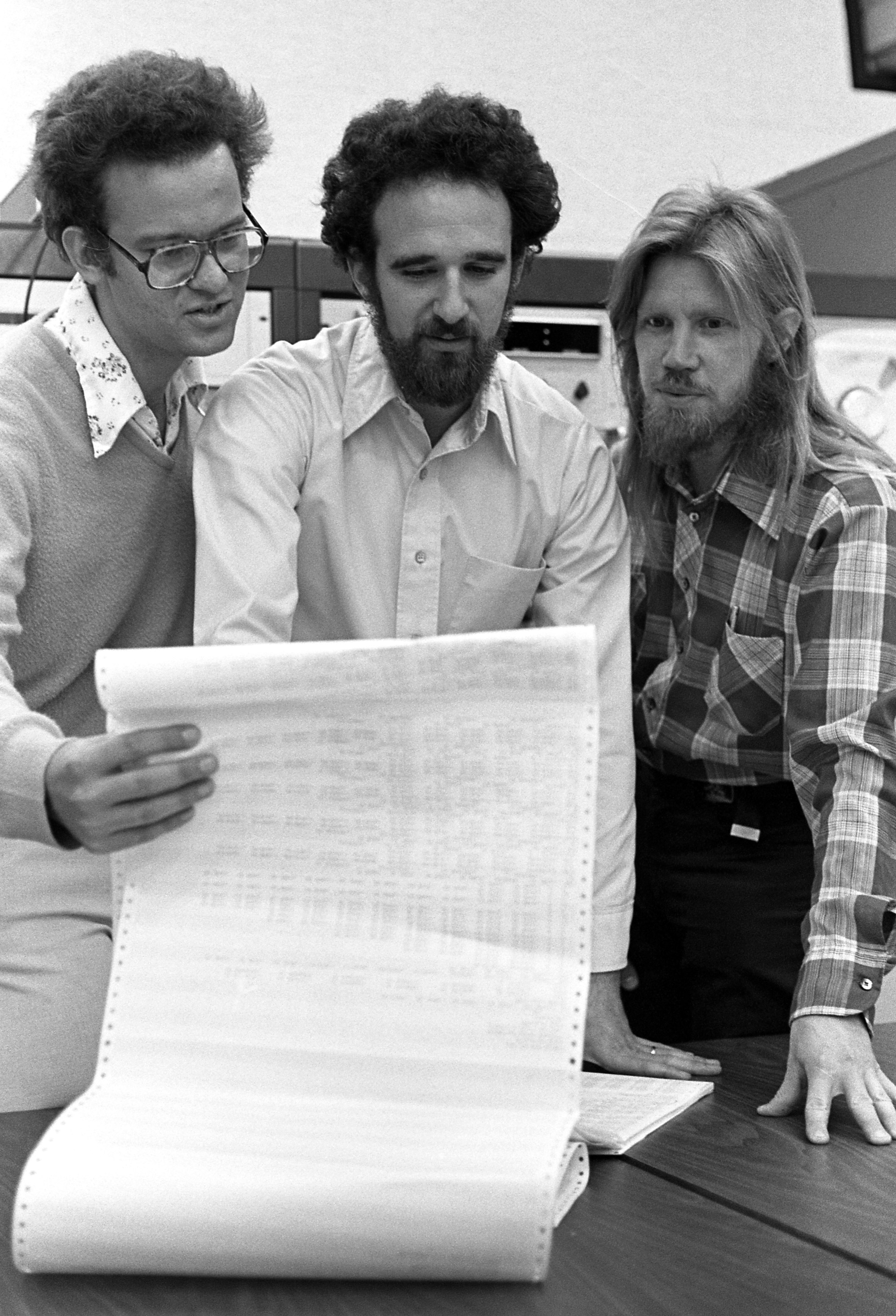 Historical photo of Ralph Merkle, Martin Hellman and Whitfield Diffie looking at a computer printout.