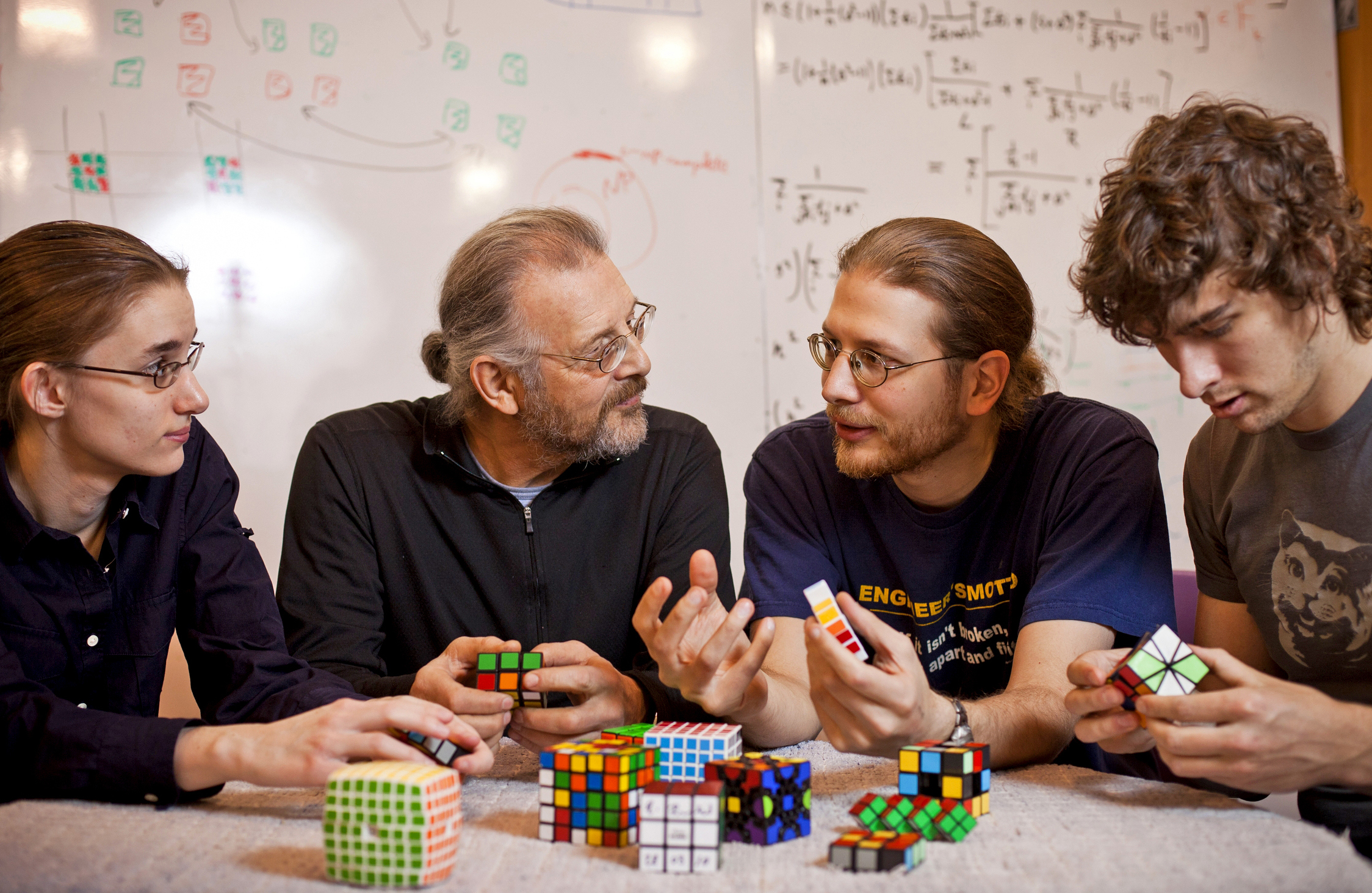 A photo of Martin and Erik Demaine, along with Sarah Eisenstat and Andrew Winslow, working with Rubik’s cubes of different sizes.