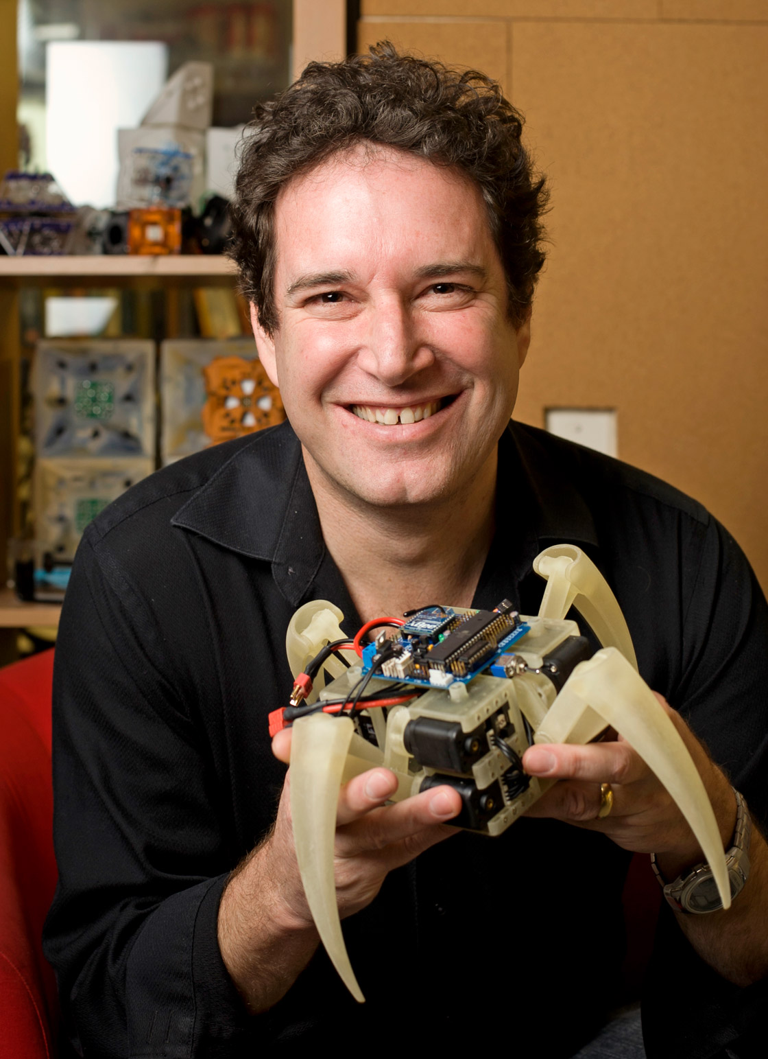 Hod Lipson smiles at the camera while holding a football-size robot resembling a spider.