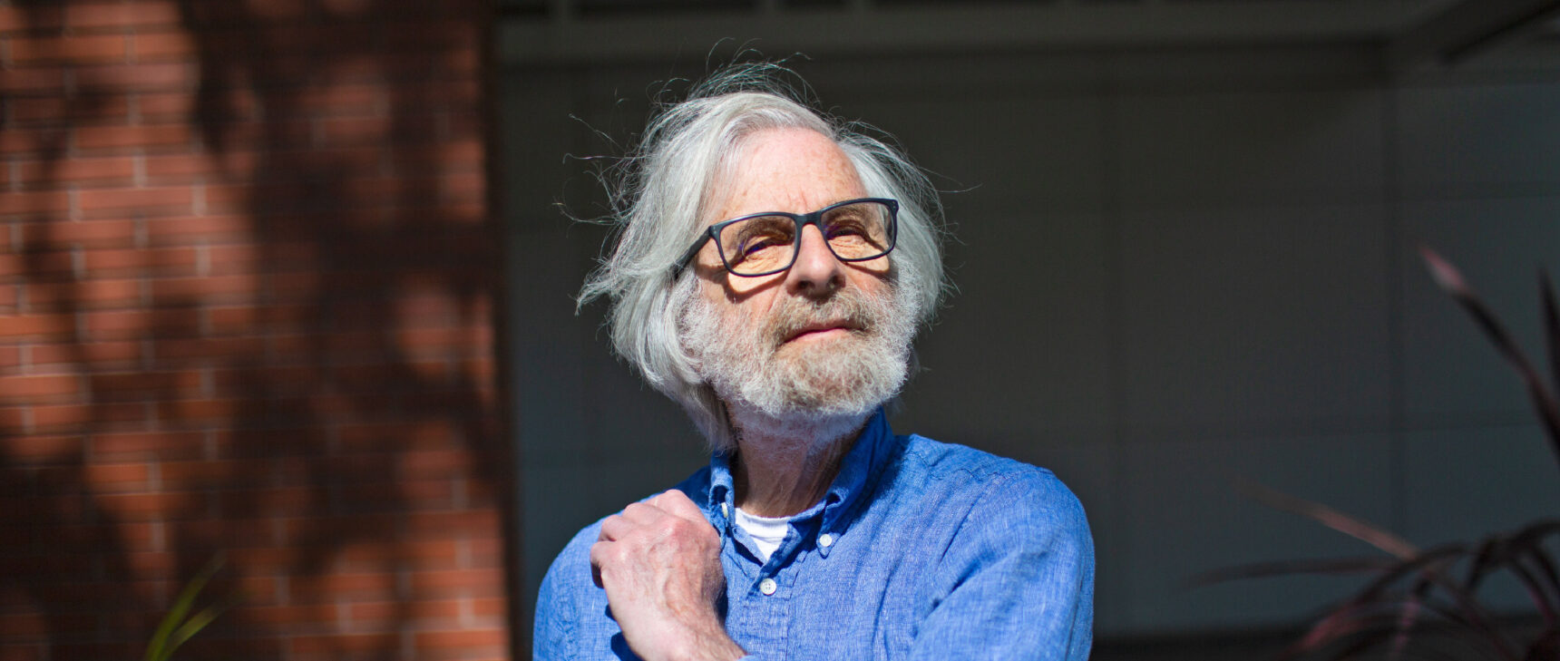 Outdoor photo of Leslie Lamport wearing a blue shirt with his hand up to his shoulder