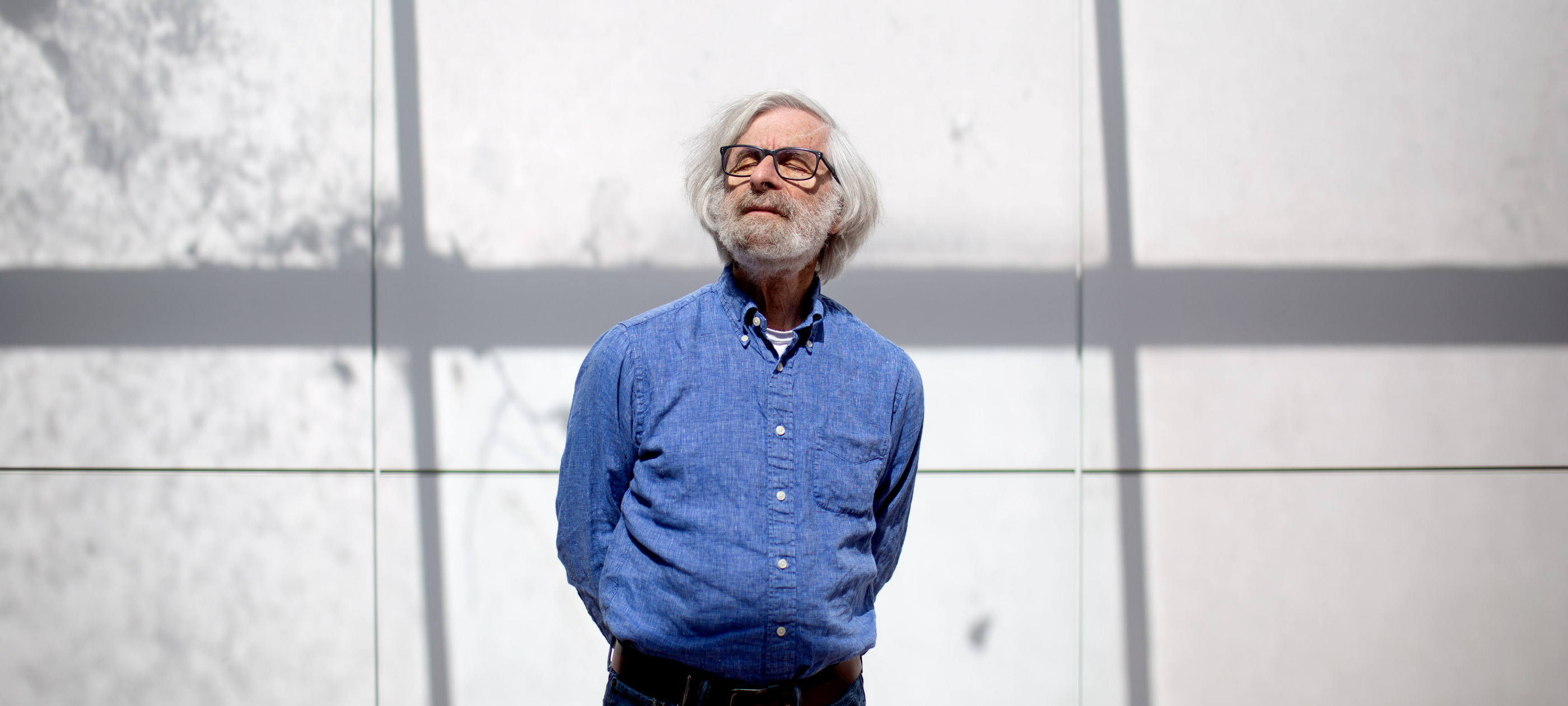 Photo of Leslie Lamport in a blue shirt standing in front of a white wall