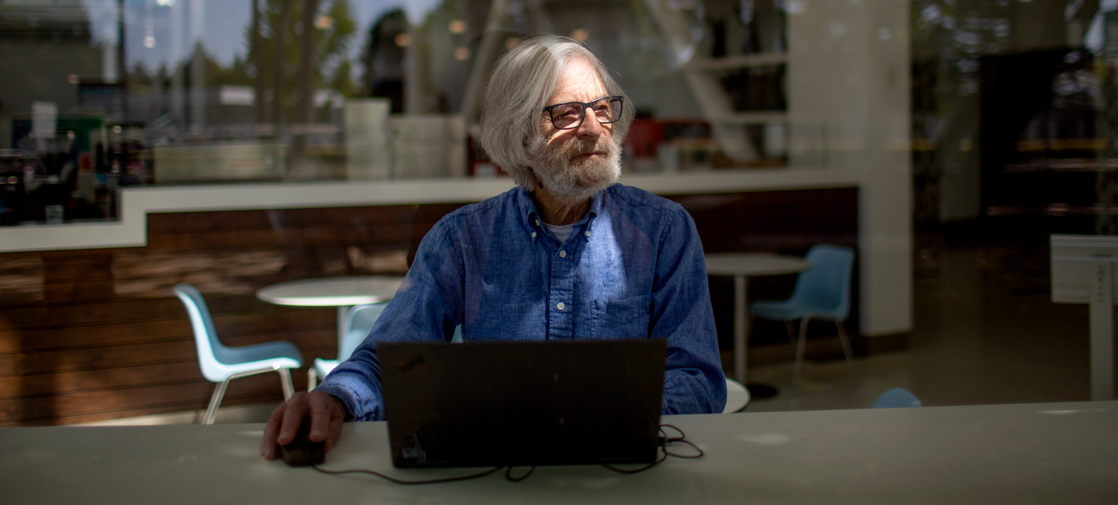 Photo of Leslie Lamport sitting at a counter using a black laptop