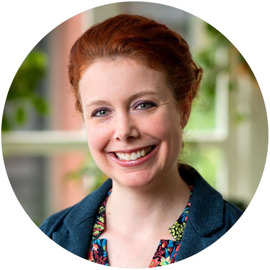 photo of a light-skinned, red-headed woman in front of a window smiling into the camera