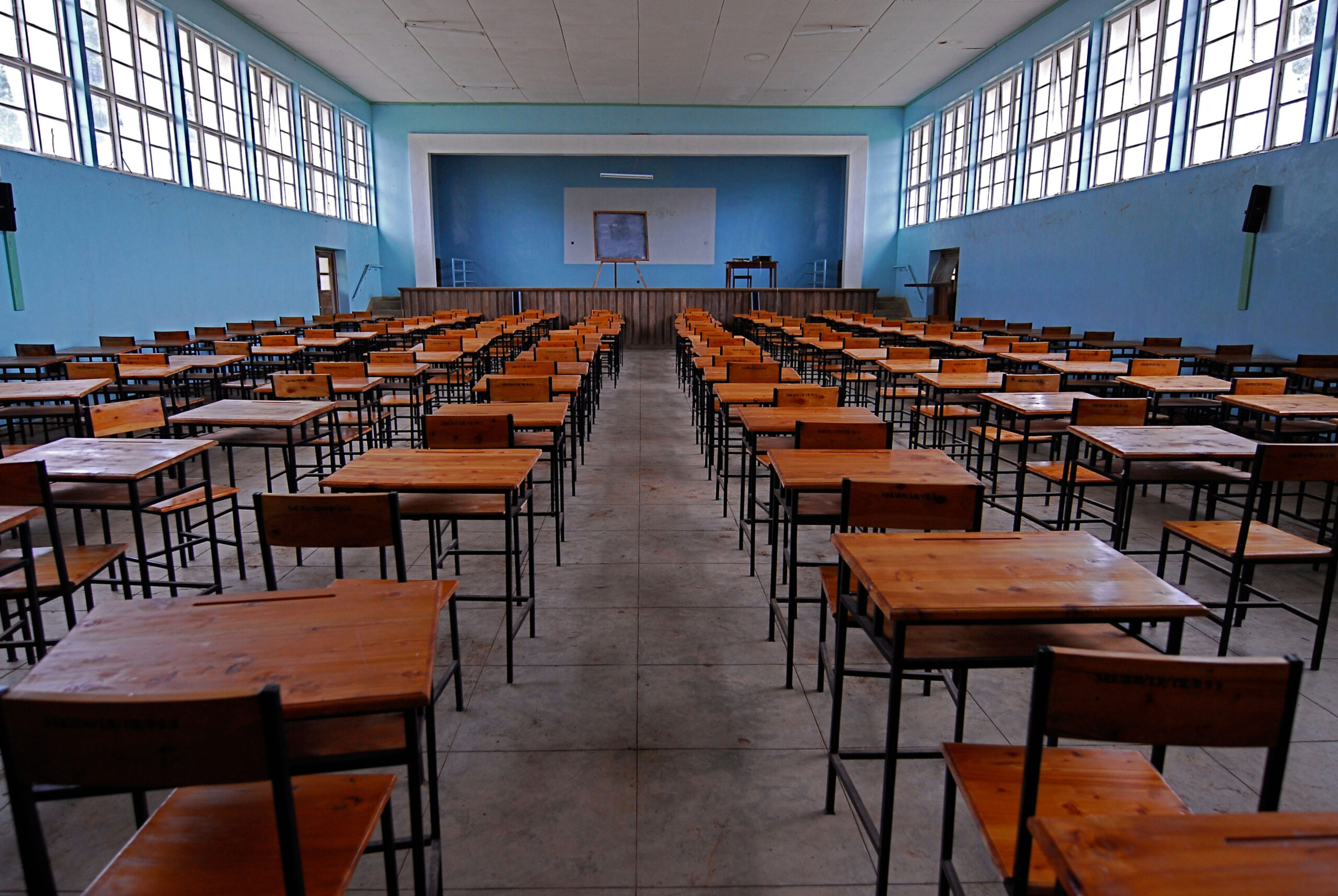 A photo of a school auditorium with blue walls and rows of empty wooden desks.