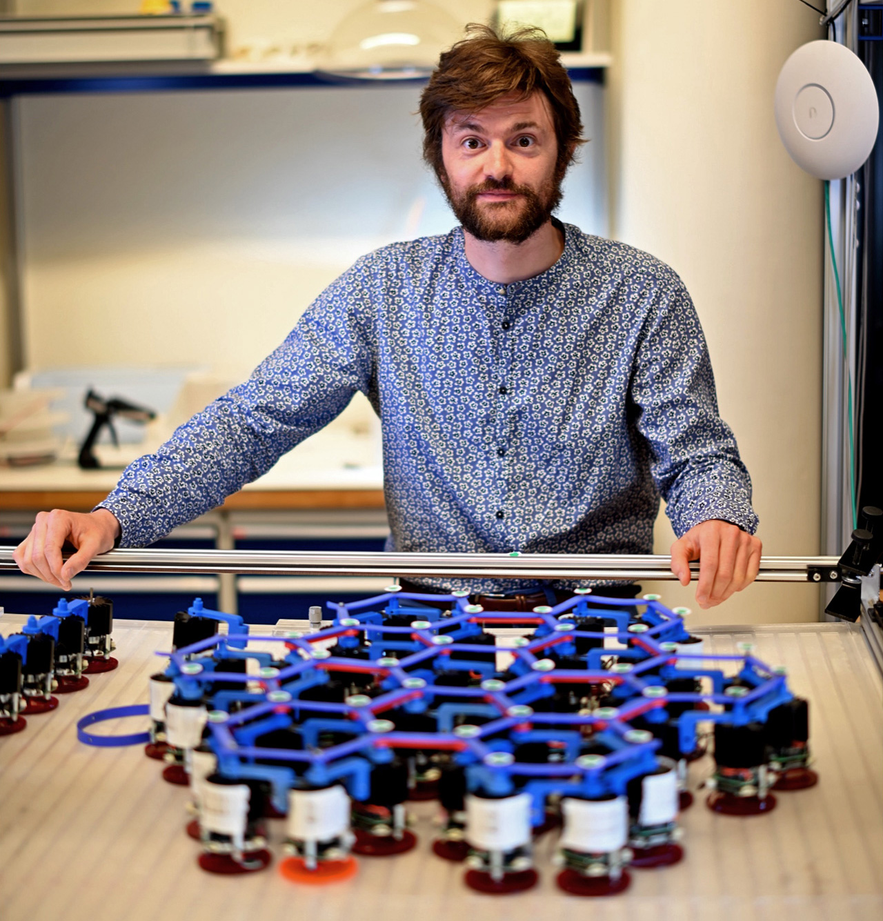 Photo of a man with a beard standing by a table of robotic modules.