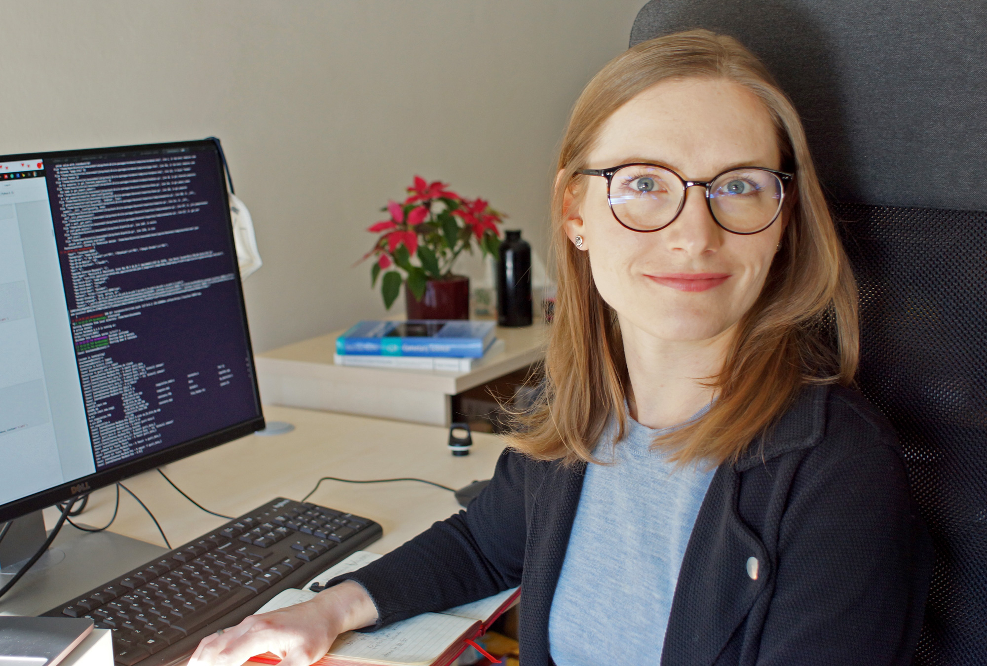 A bespectacled woman sitting at a computer and turning and smiling toward the camera.