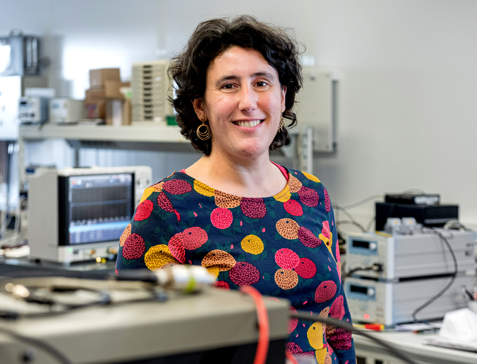 A woman stands in a lab wearing a floral shirt.