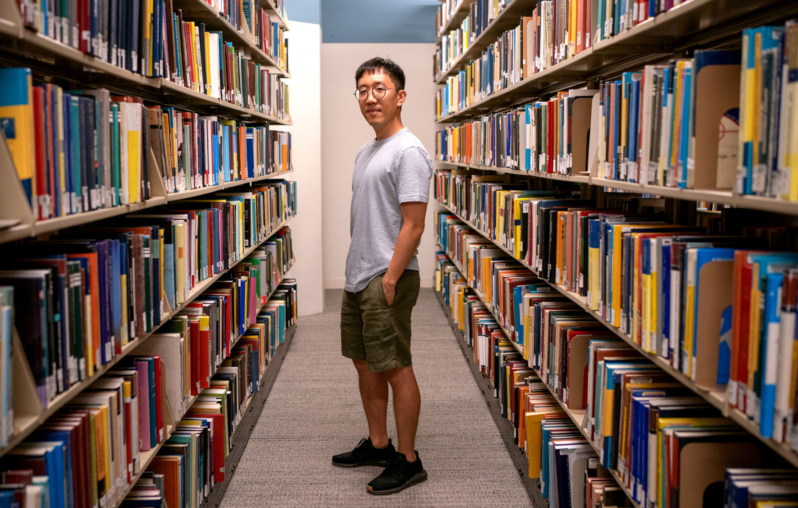 June Huh stands between bookshelves.