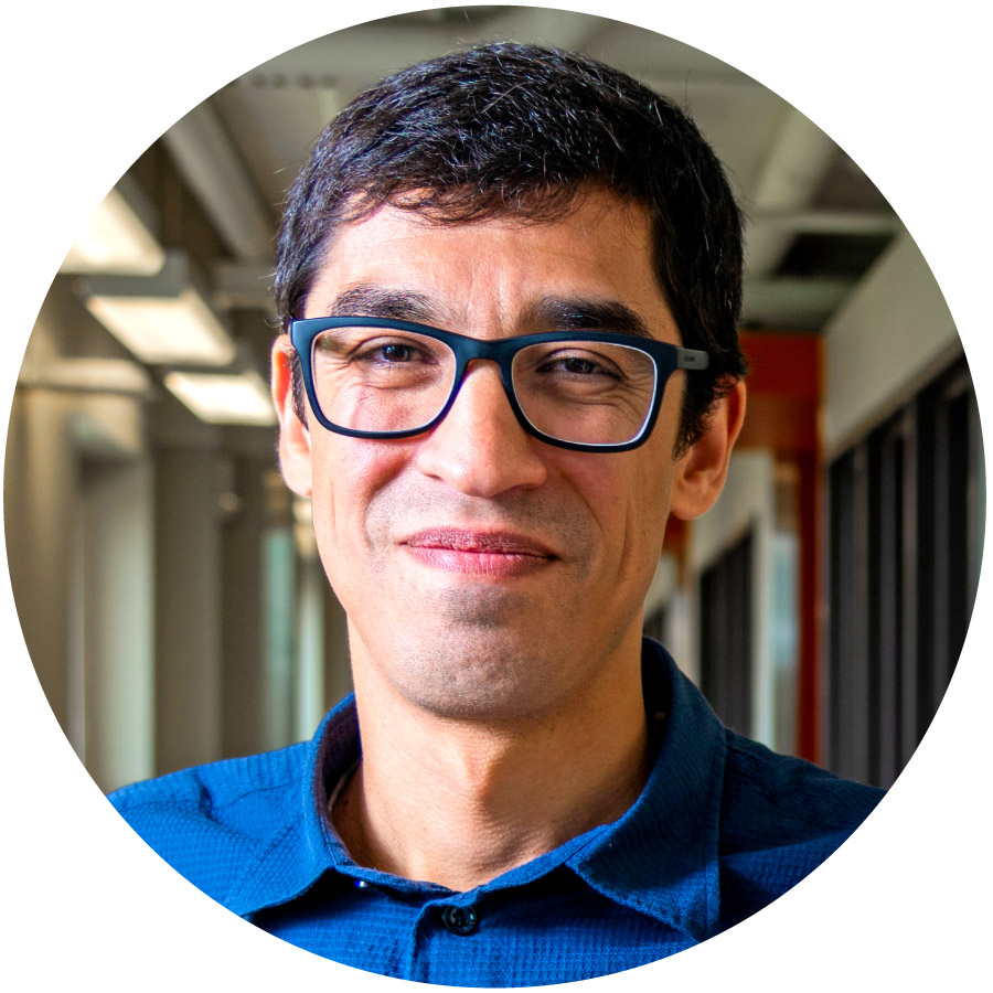 photo of a man with dark hair and glasses and a blue shirt smiling into the camera