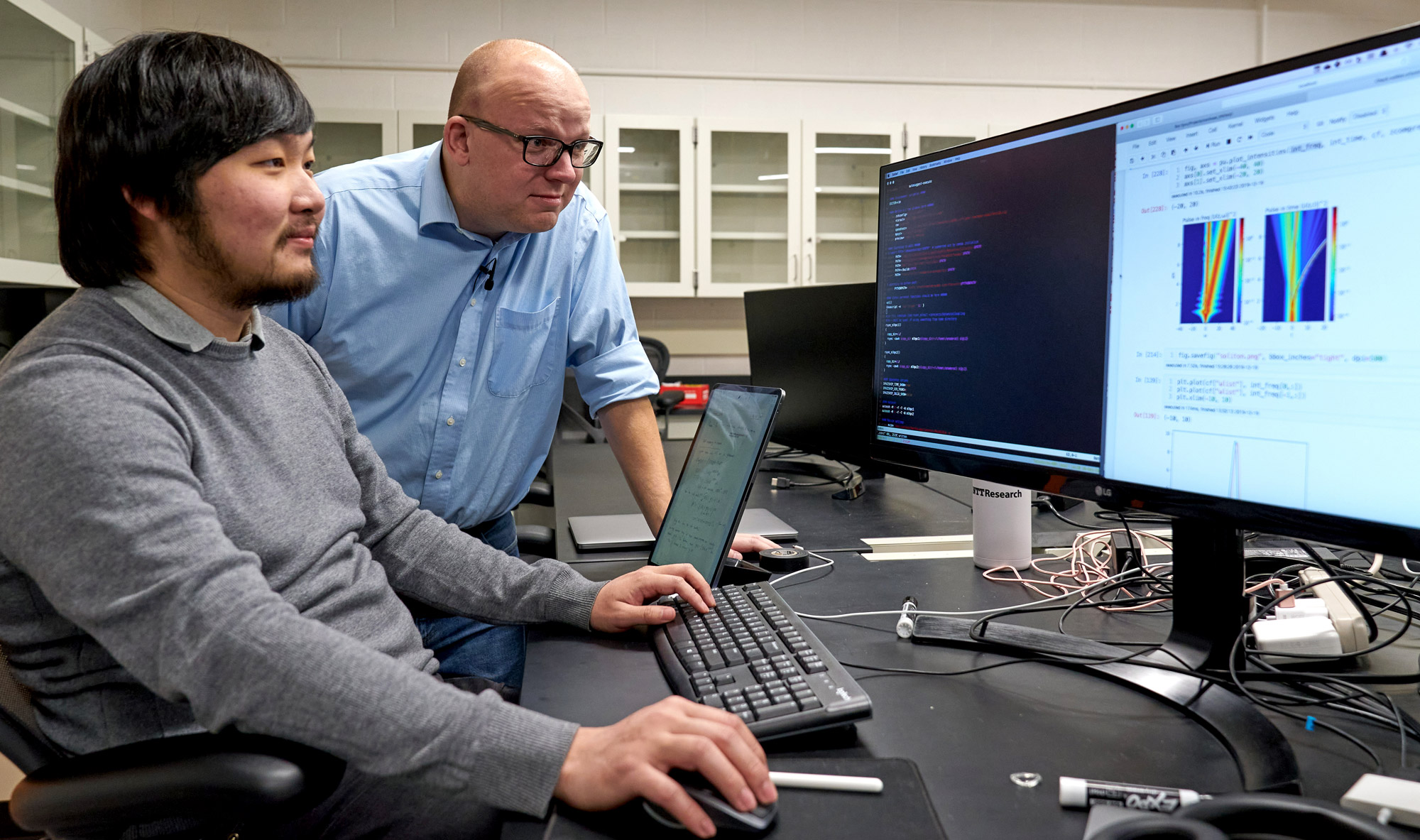 Two men look at a computer screen.