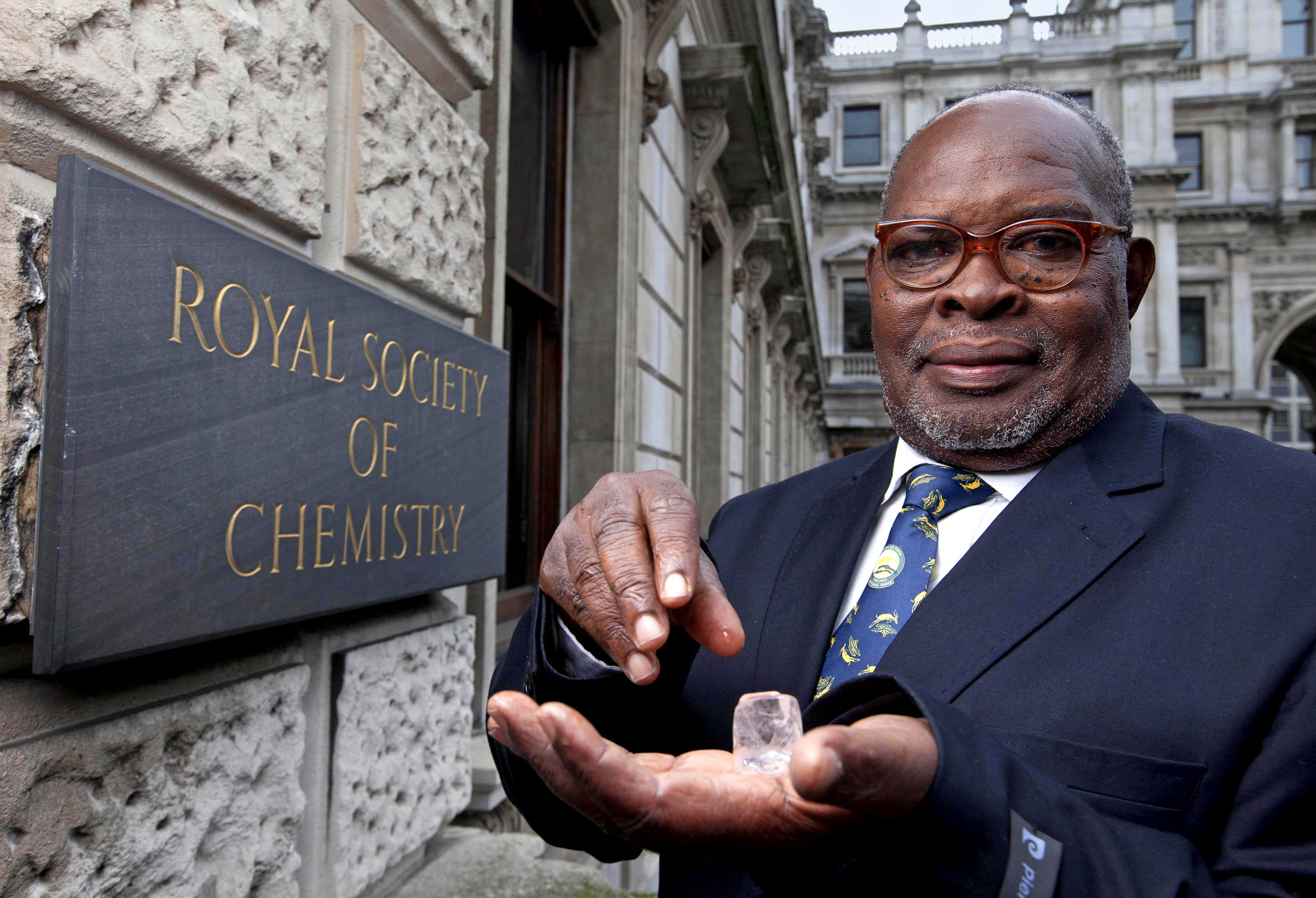 A middle-aged man in a suit holding an ice cube in his palm