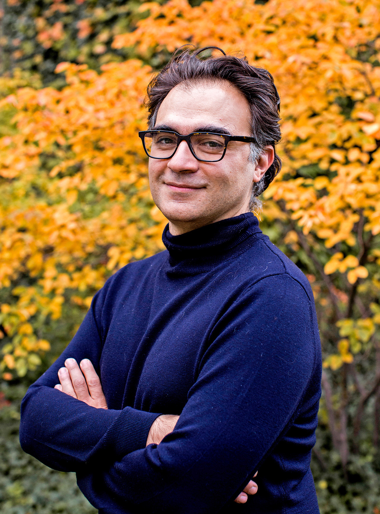 Photo of a man in glasses standing in front of a tree