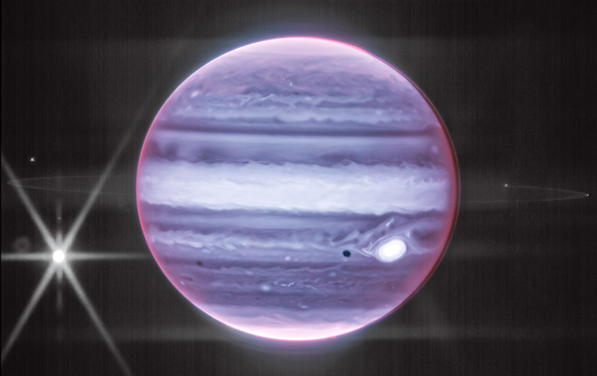 Jupiter appears purple-blue, with white stripes; a thin ring encircles the planet, and one of its moons shines brightly to its left