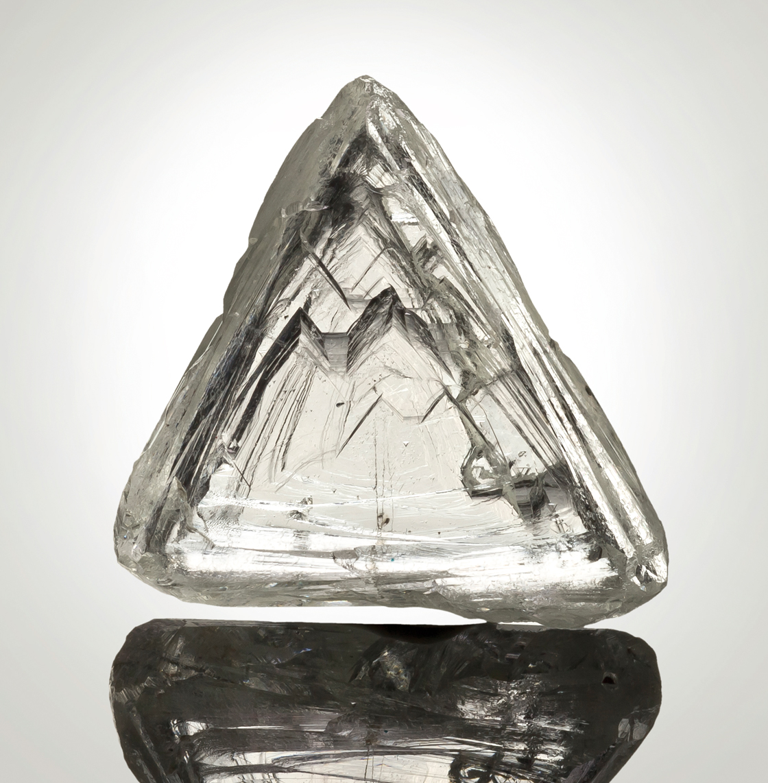 close up of a triangular, roughly cut diamond agains a glowing background.