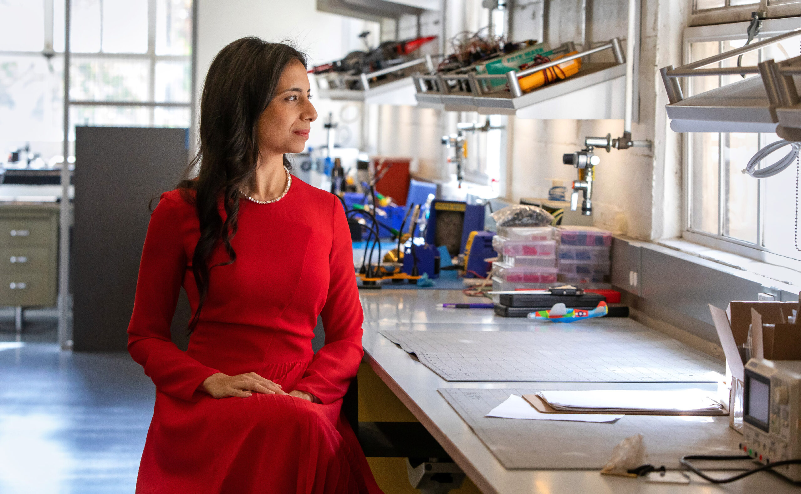 Anima Anandkumar in a red dress sitting at a bench in a lab