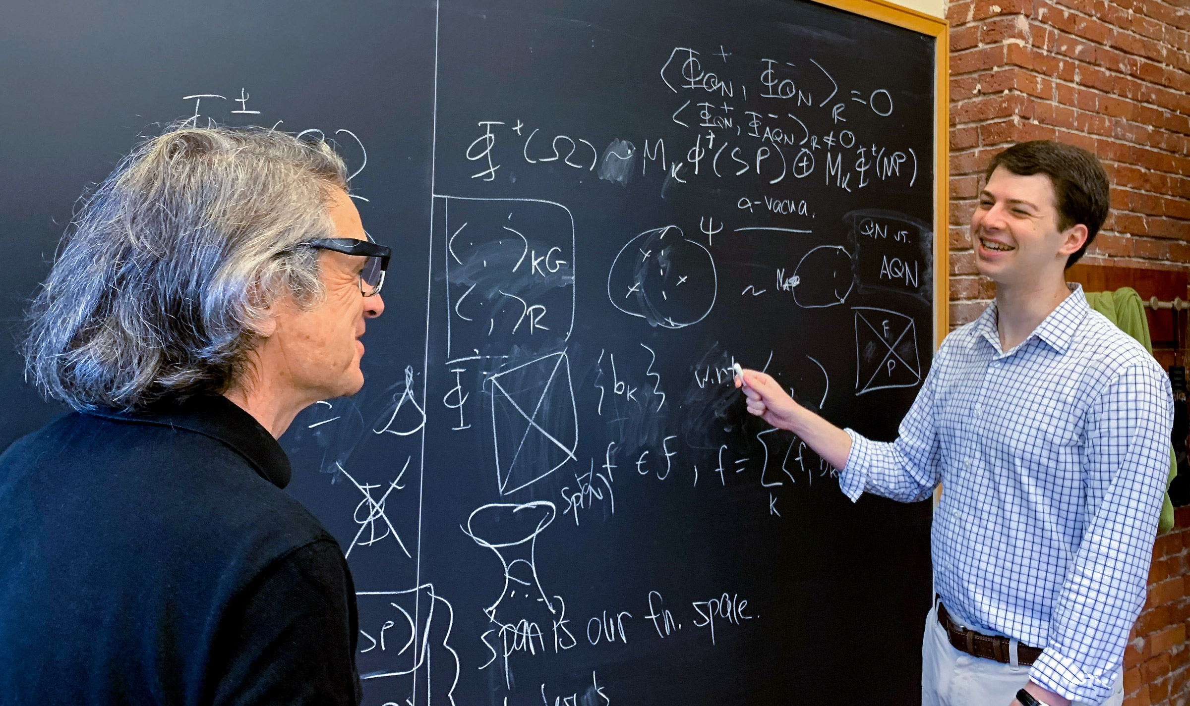 Two men smile at each other from either end of a blackboard.