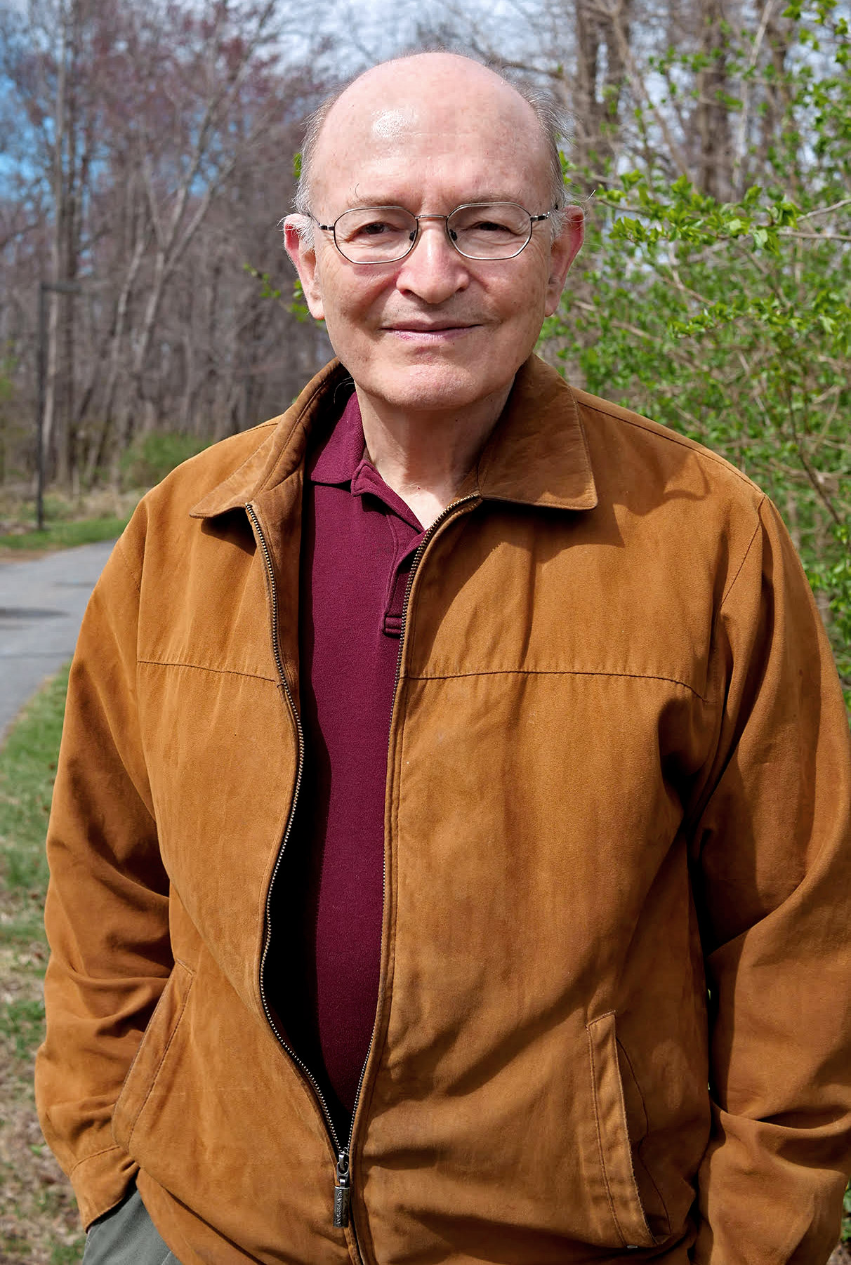 Portrait of a bald man in glasses standing outside.