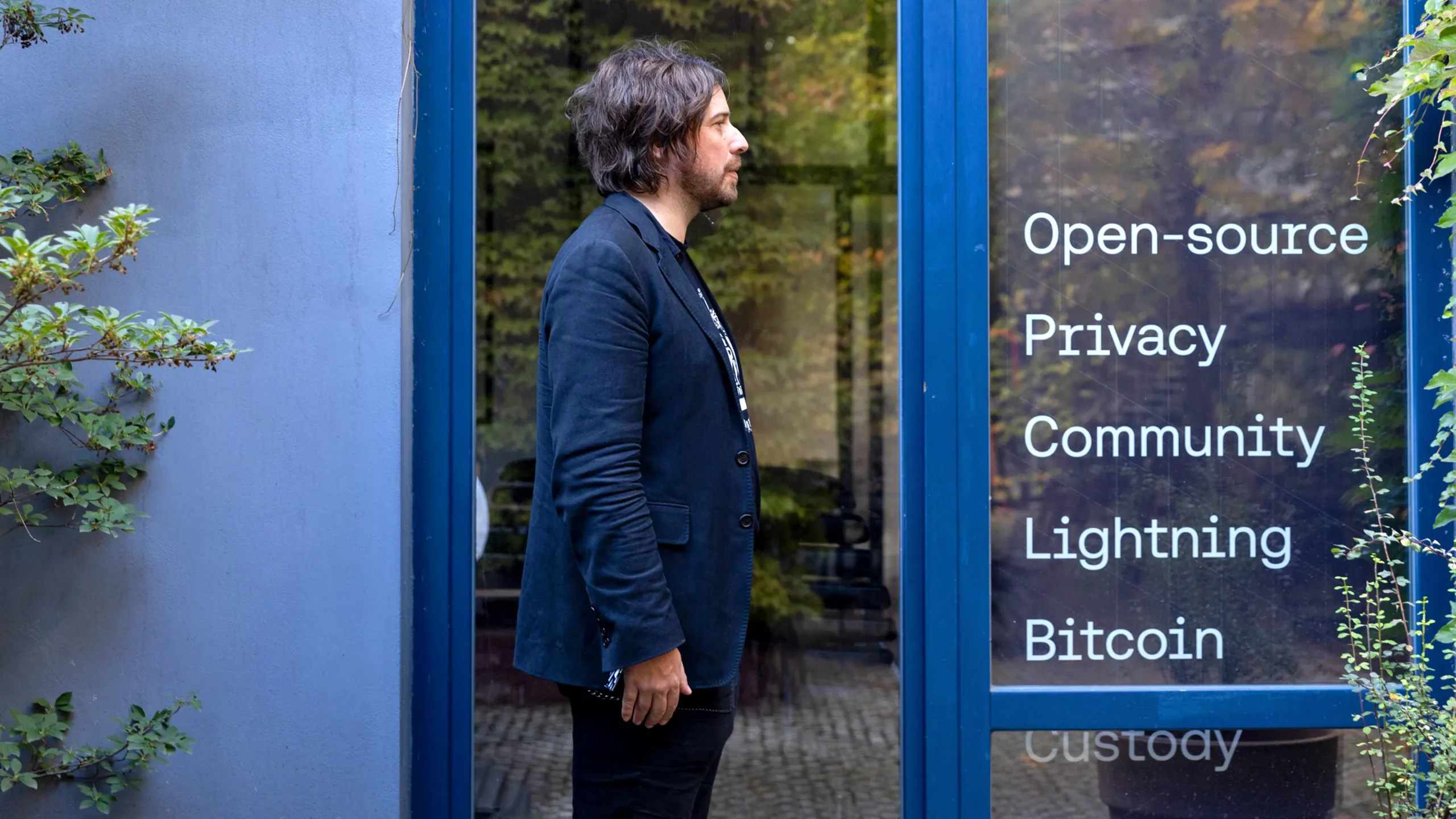 Harry Halpin stands in profile in a blue doorway, facing words printed on a window