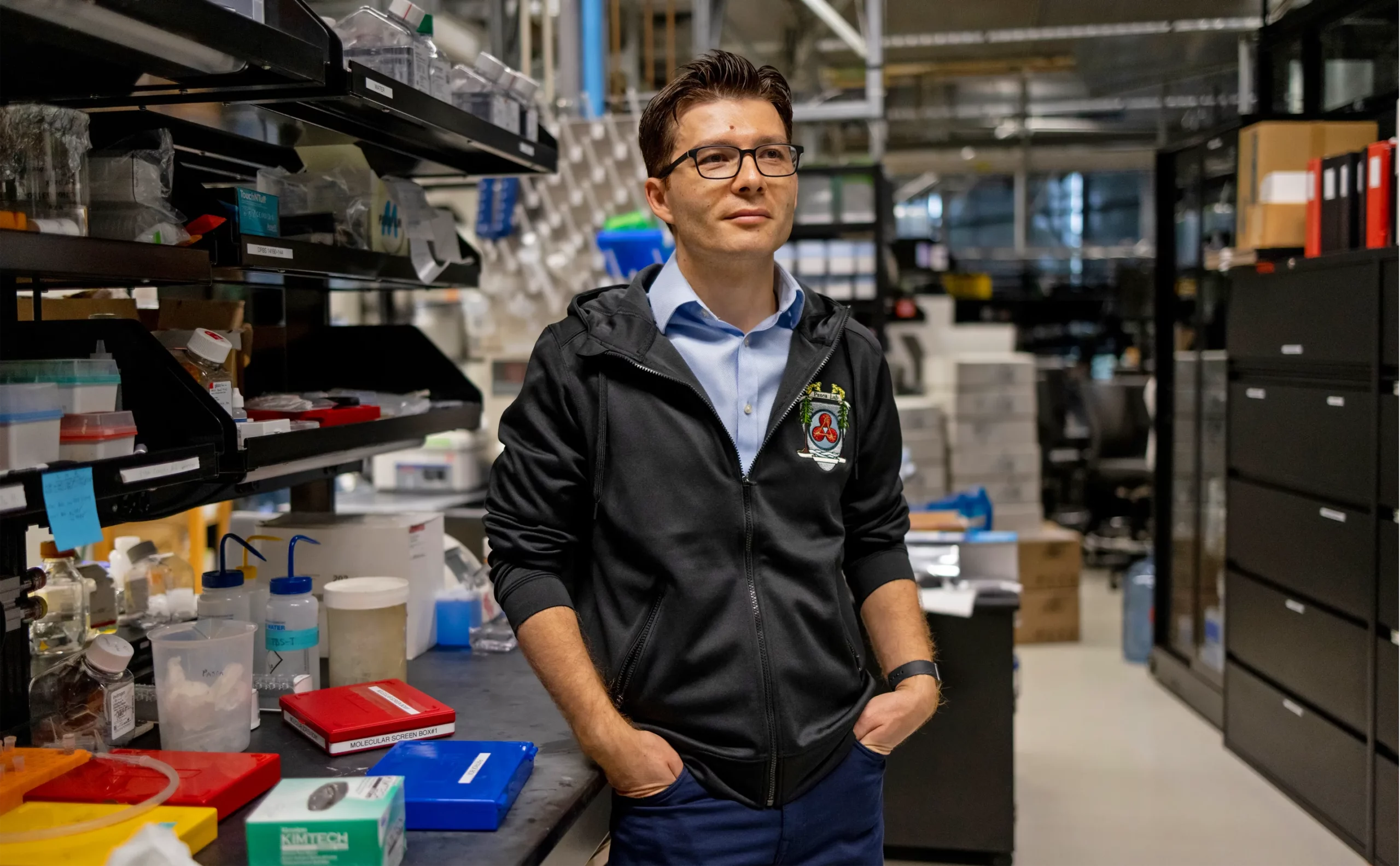 Sergiu Paşca standing in his lab at Stanford University beside a bench and shelves littered with equipment.