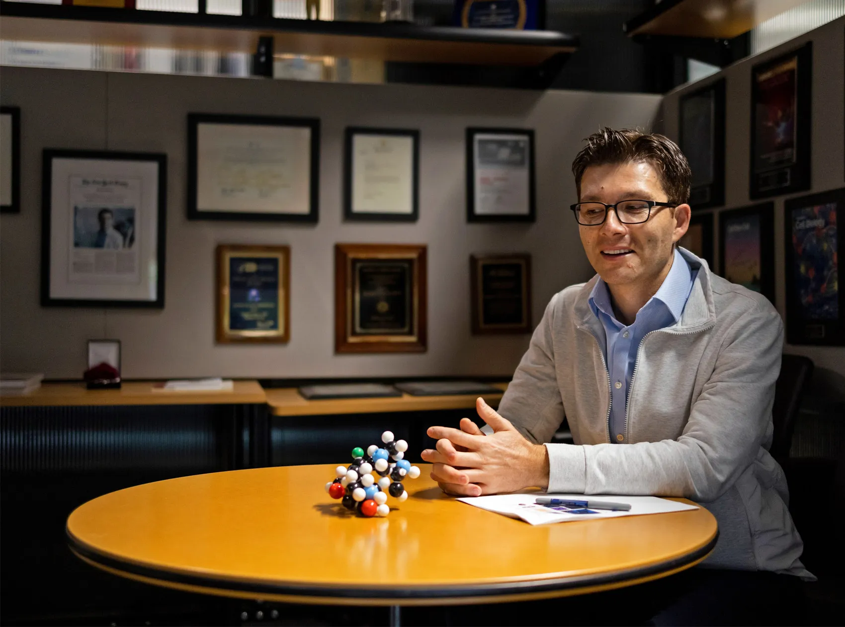 Sergiu Paşca sits with his hand folded at a table that holds a model of a molecule.