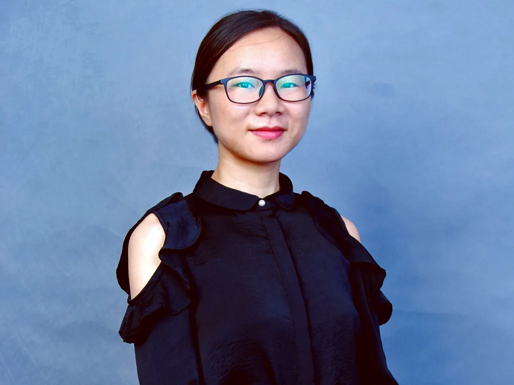 Xuemei Gu in a black outfit in front of a gray background