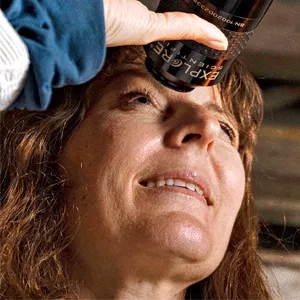 Lisa Kaltenegger, a woman with red hair, peers through the eyepiece of an antique telescope.