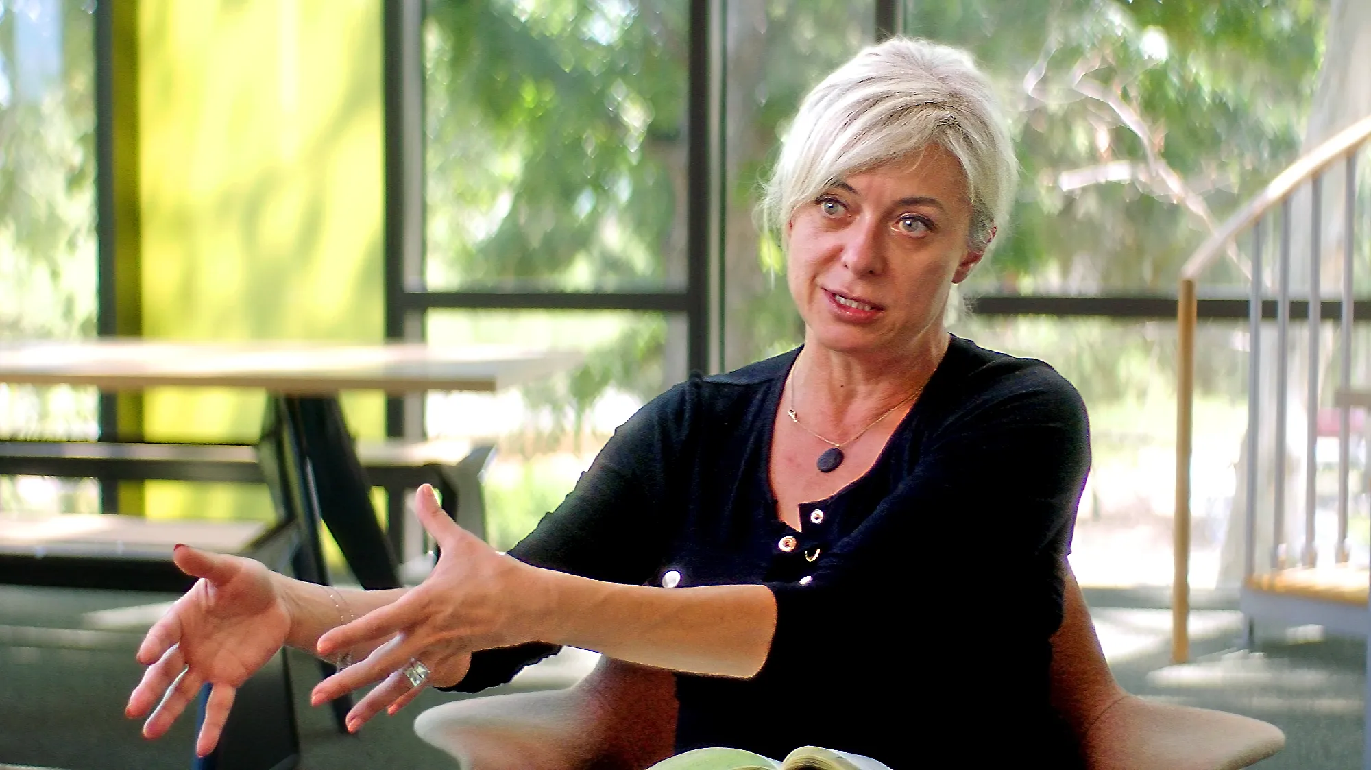 Candid shot of a woman with bleach-blonde hair in a black sweater talking and gesturing.