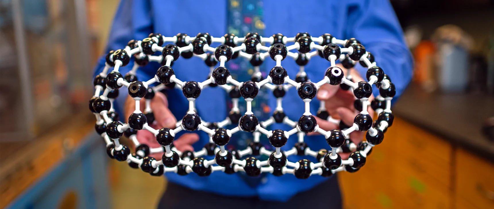 Hands hold a ball-and-stick model of a pill-shaped molecule called a fullertube.