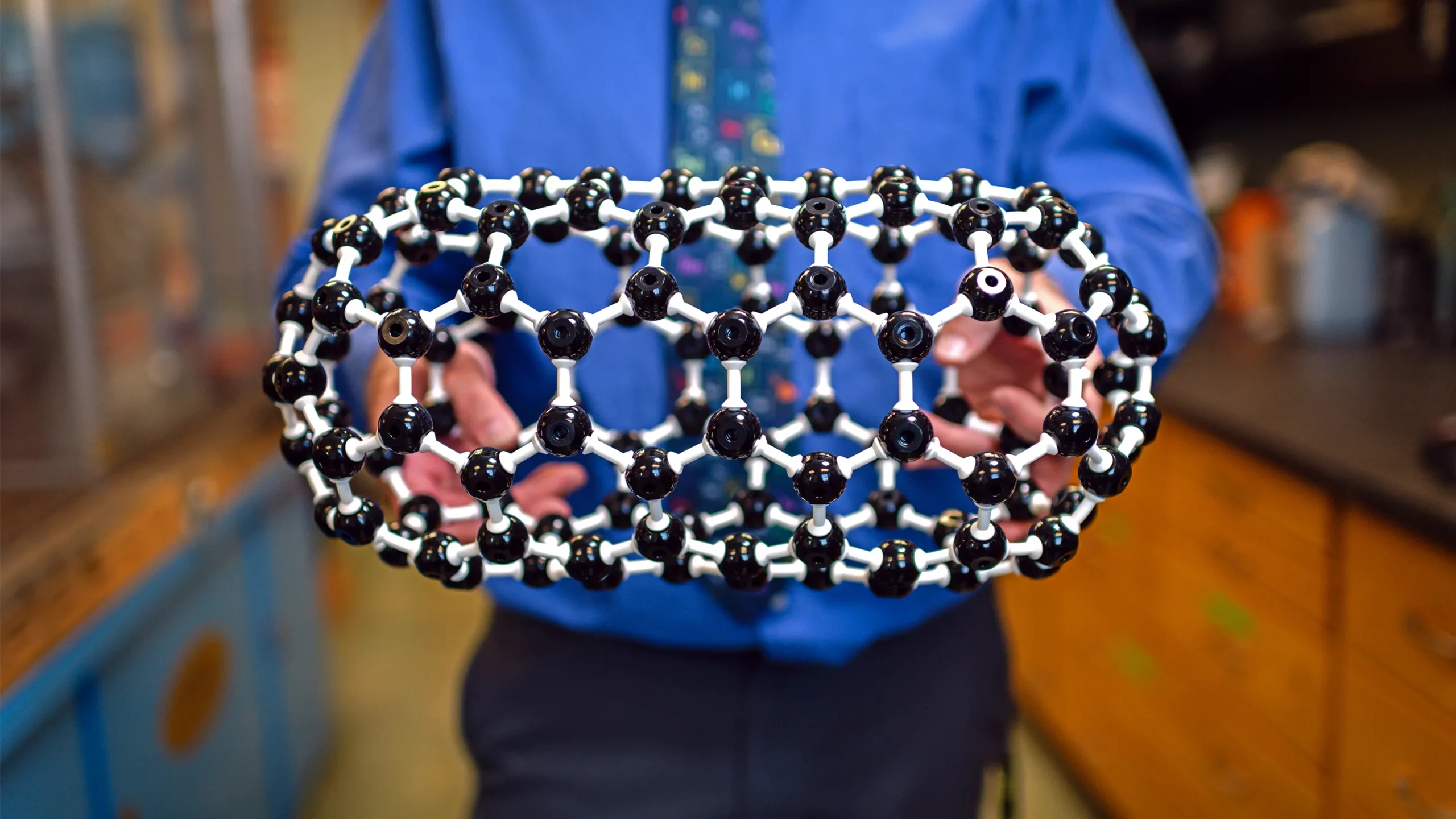 Hands hold a ball-and-stick model of a pill-shaped molecule called a fullertube.