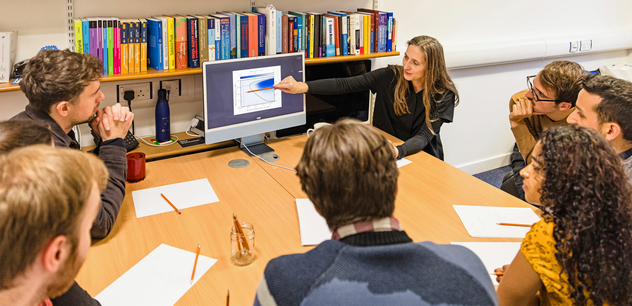 A candid photo of Weinfurtner and several students seated around a table, as she gestures to a plot on a computer screen.